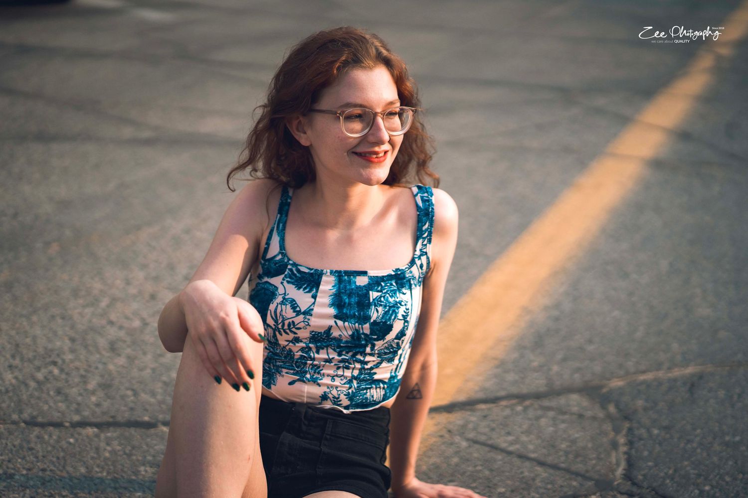 Candid outdoor portrait of person in blue patterned top sitting on ground.
