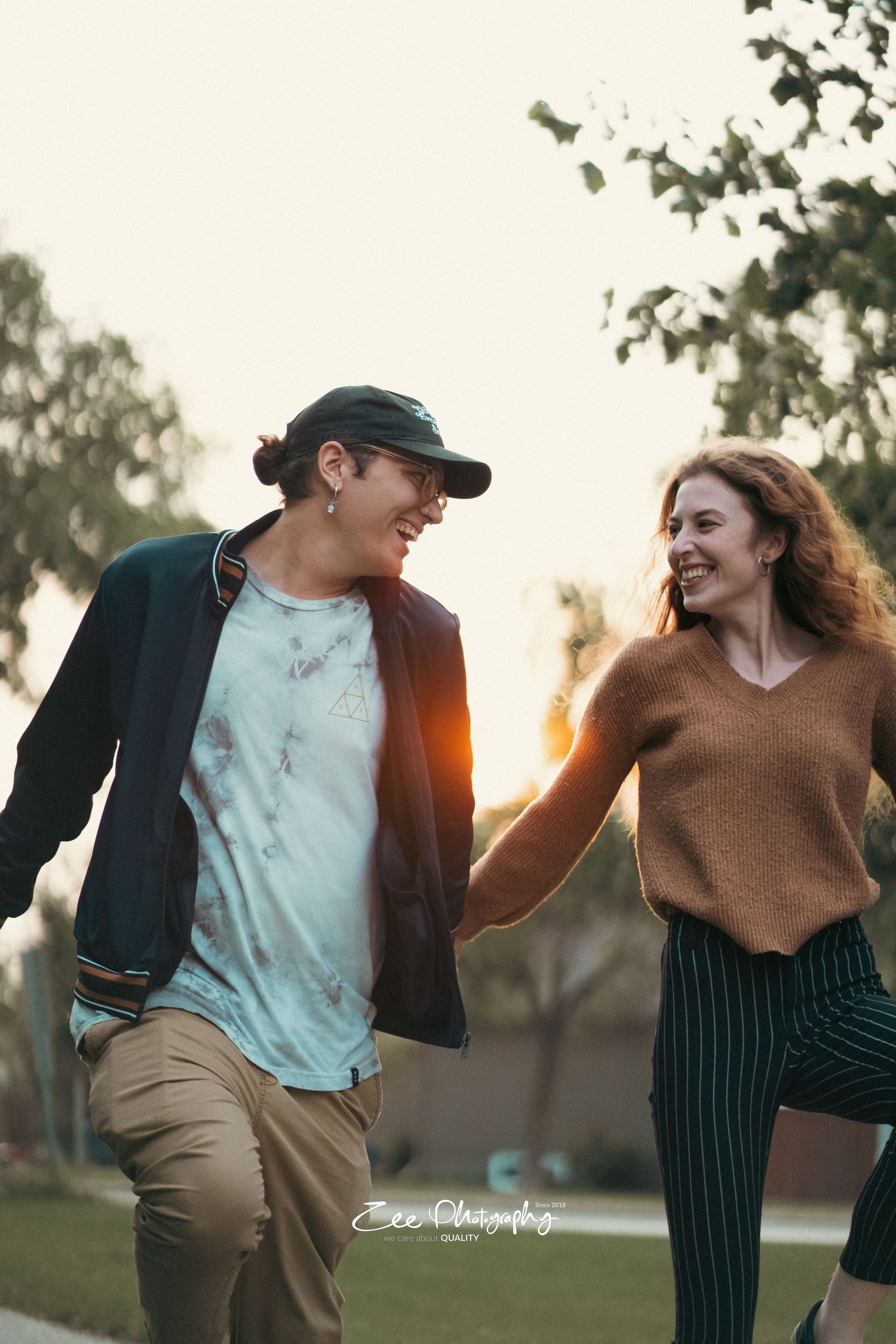 Couple in casual wear walking and laughing together on a path at dusk.