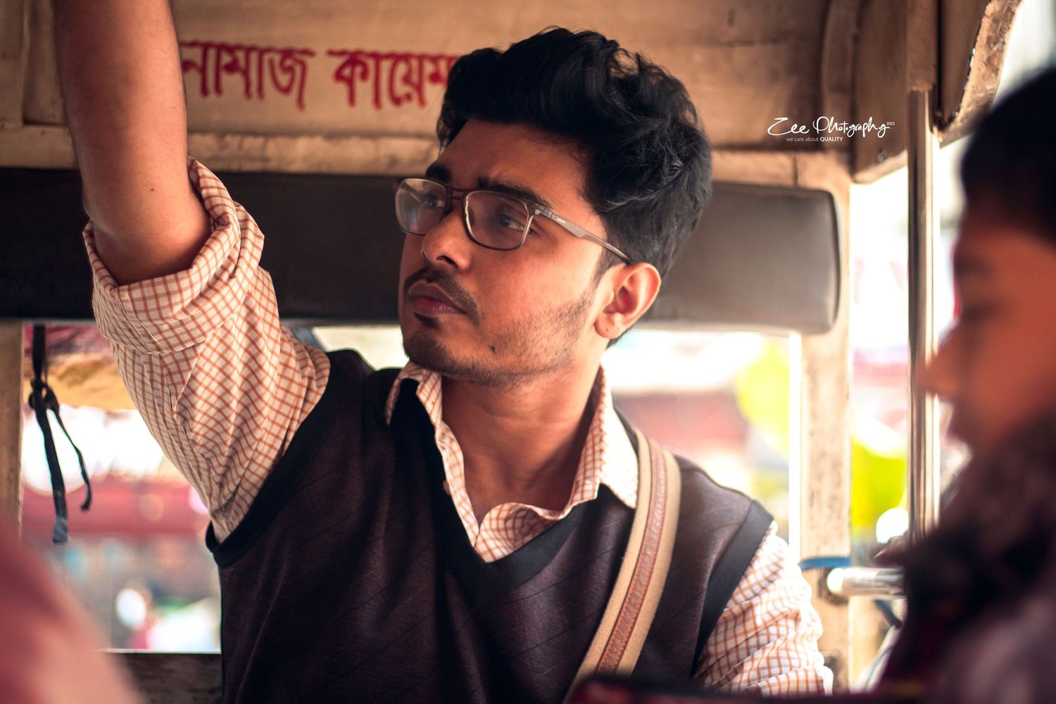 A young student wearing glasses and a sweater vest rides on public transportation in India.
