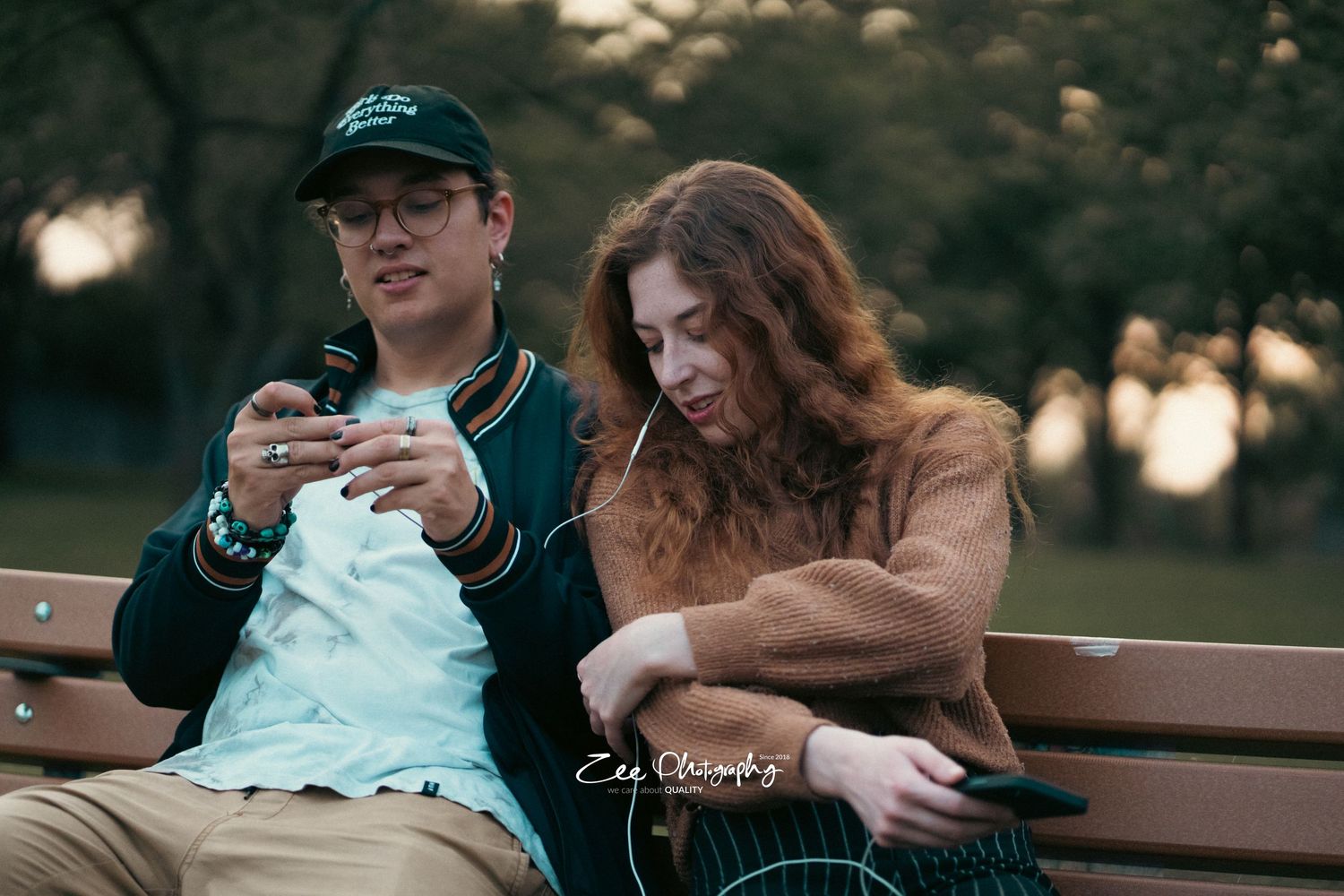 Couple sitting together on park bench during sunset looking at phone.