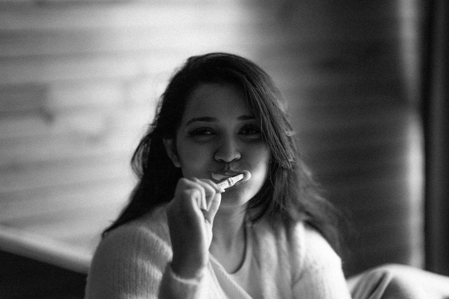 Black and white portrait of someone in a cozy sweater smiling warmly while resting their hand near their face.