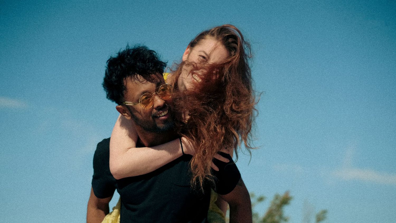 A couple embracing and laughing together against a blue sky background during a sunny day.
