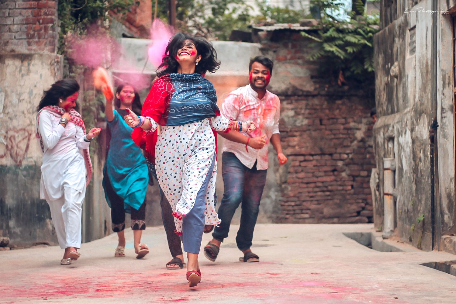 Group celebrating Holi festival with colorful powder in an alleyway.