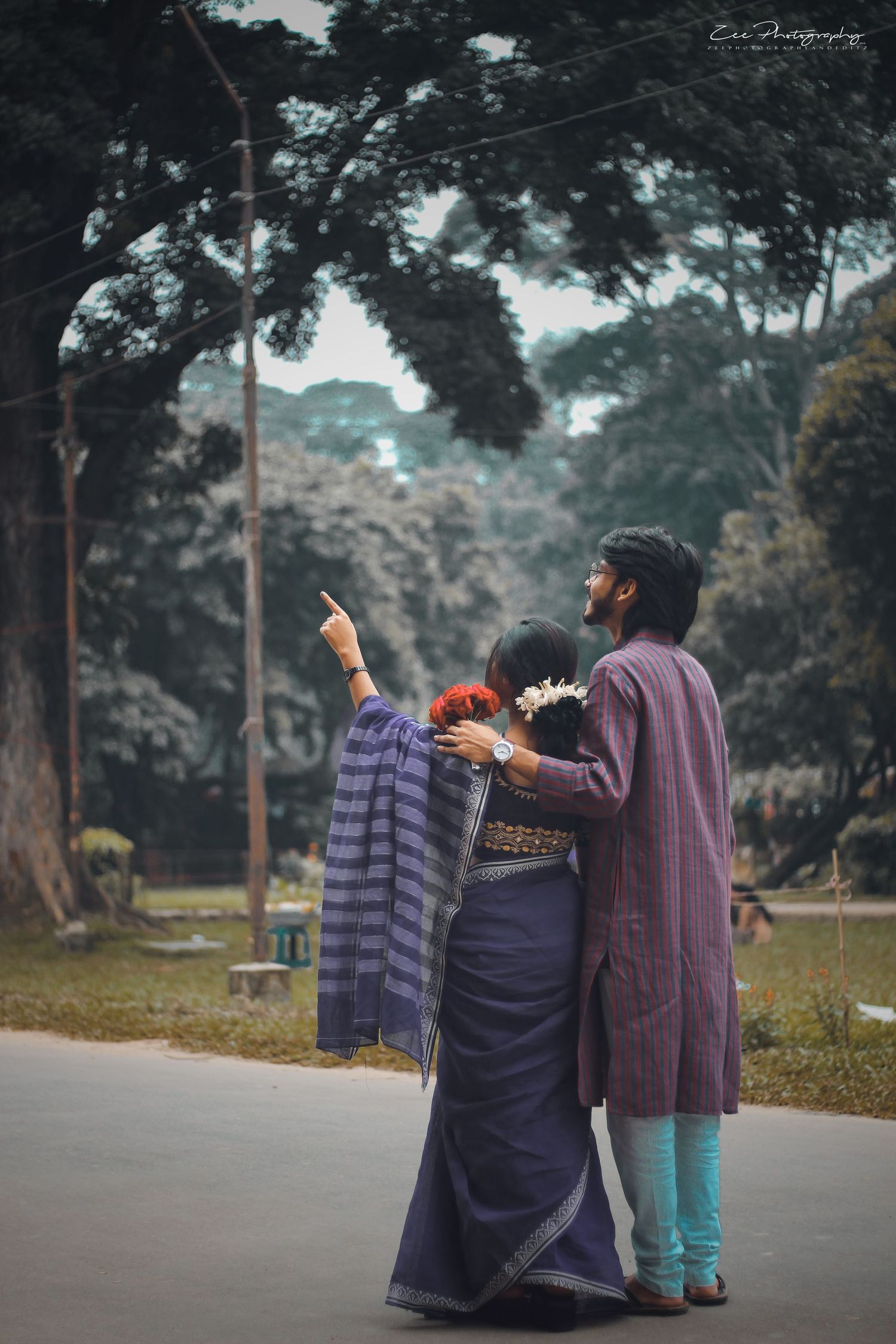 Couple in purple attire walking together on a misty path surrounded by trees.