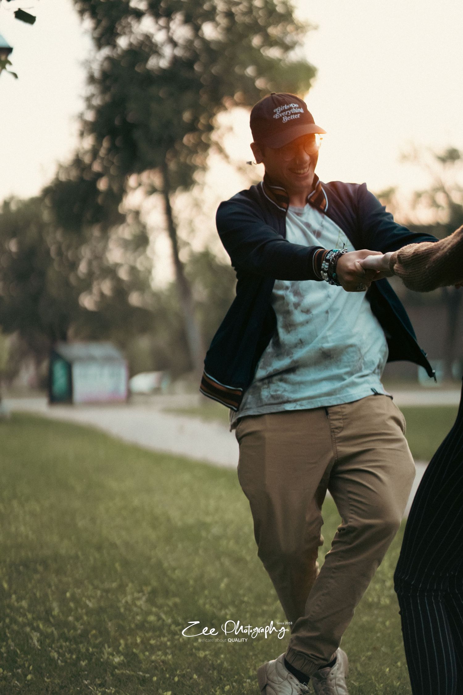 Person in baseball cap and jacket dancing playfully in a park setting.