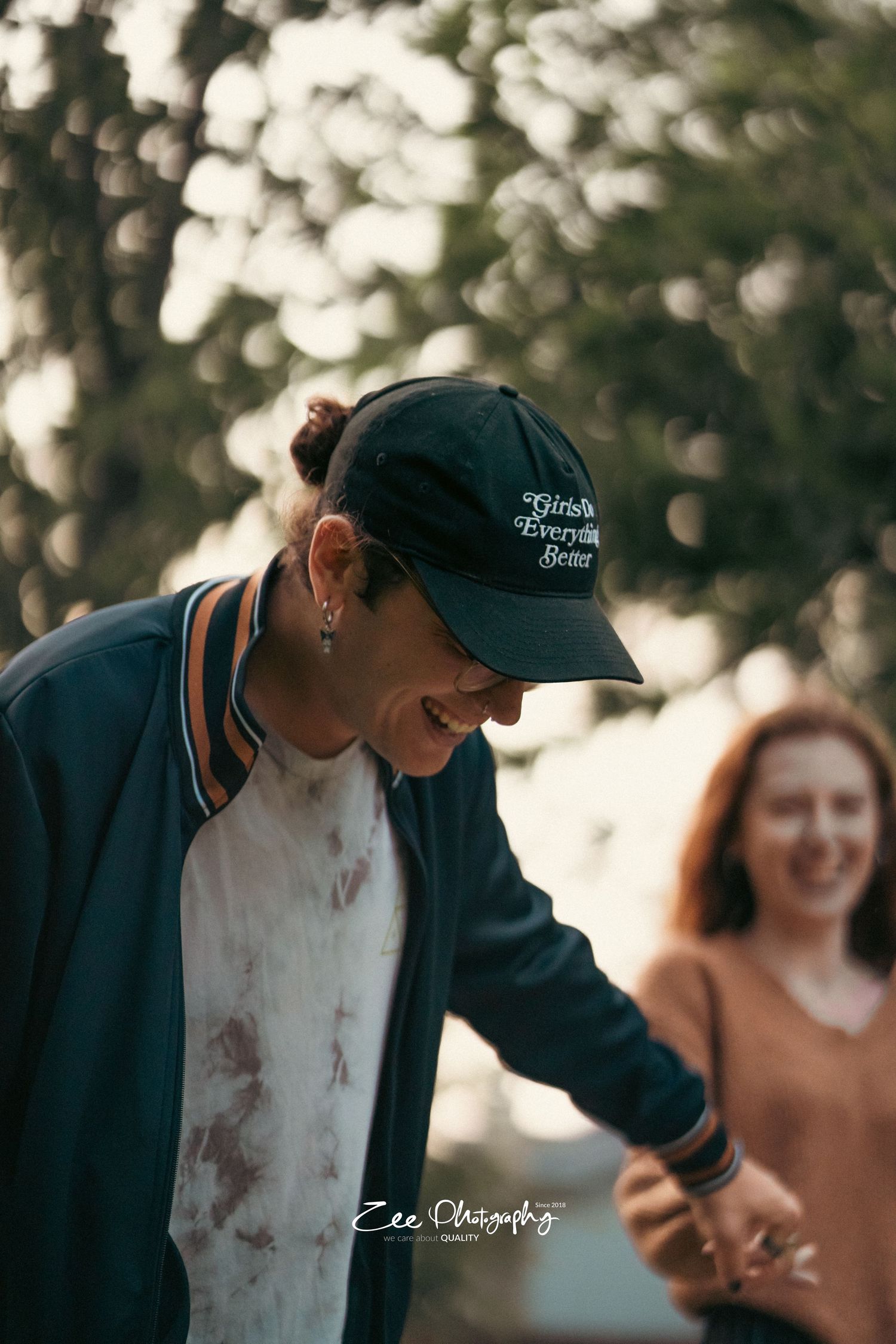 Person in baseball cap smiling while dancing outdoors during sunset.