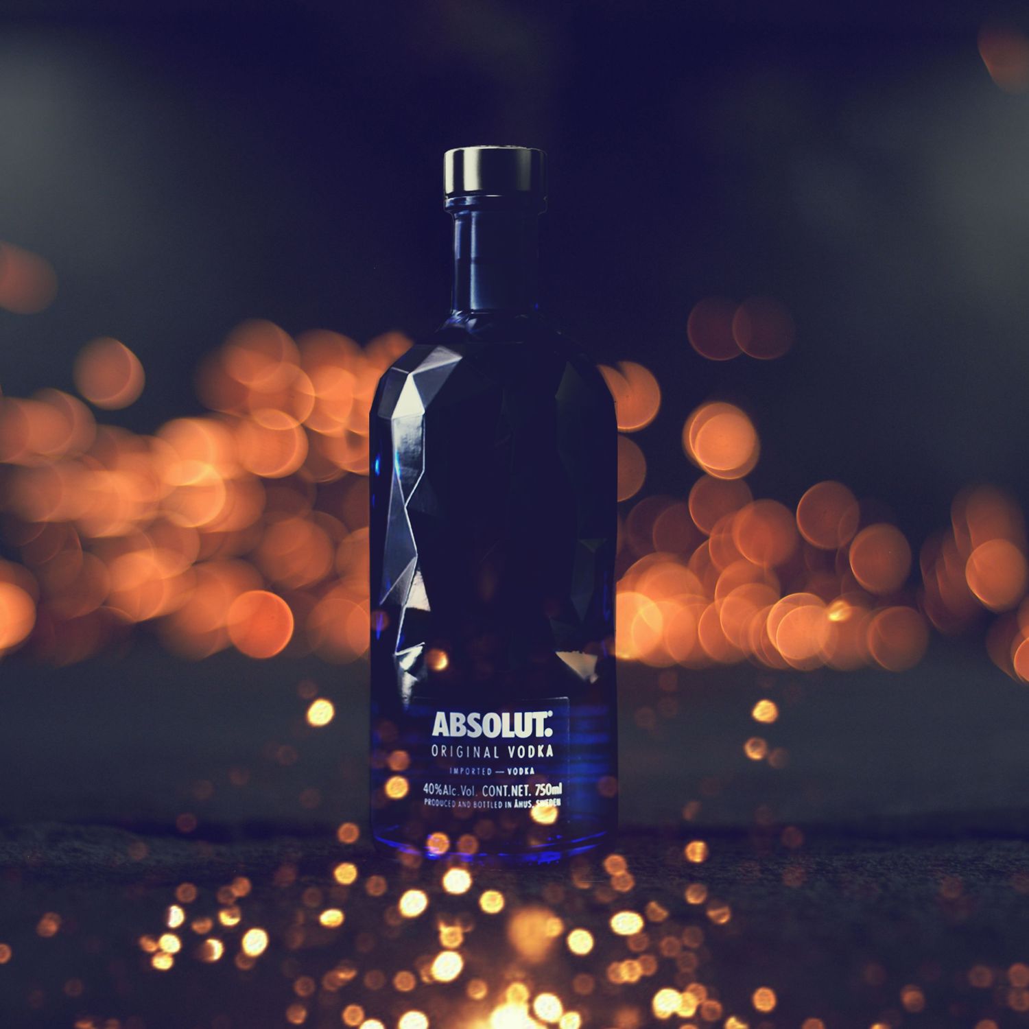 Absolut vodka bottle against dark background with blurred orange bokeh lights creating moody ambiance.
