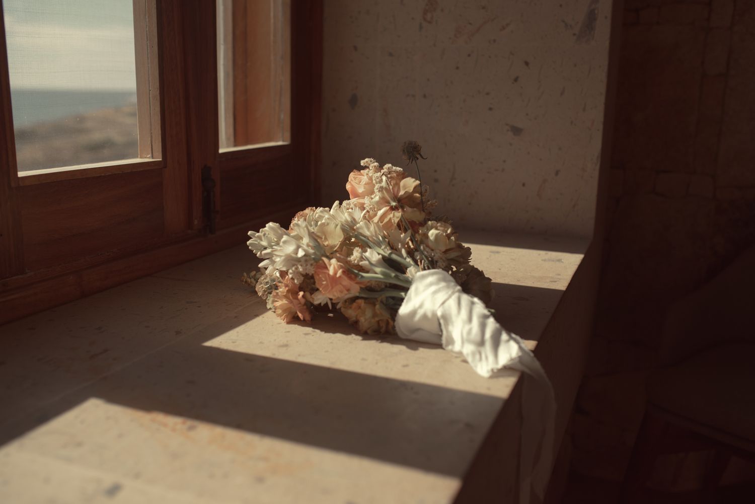 A wedding bouquet of dried flowers resting on a windowsill in warm sunlight.