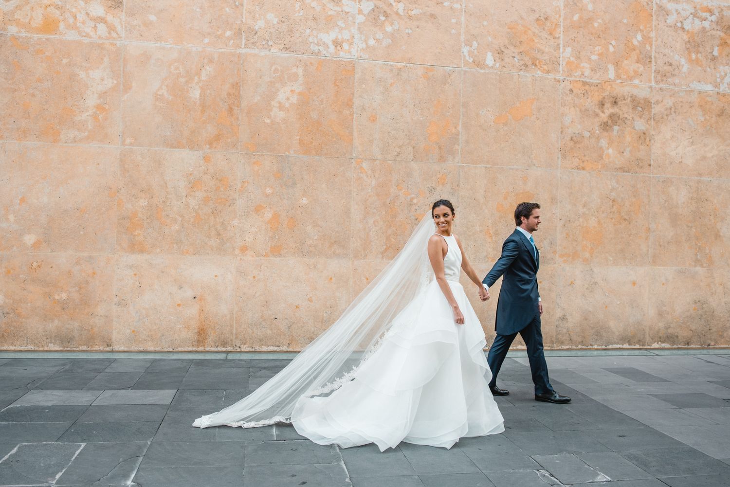 Wedding couple walking along a stone wall during their portrait session.