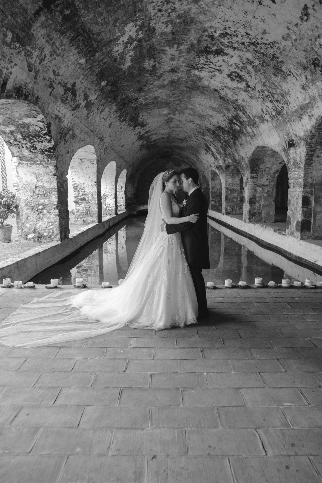 Wedding couple embracing under stone archway in black and white.