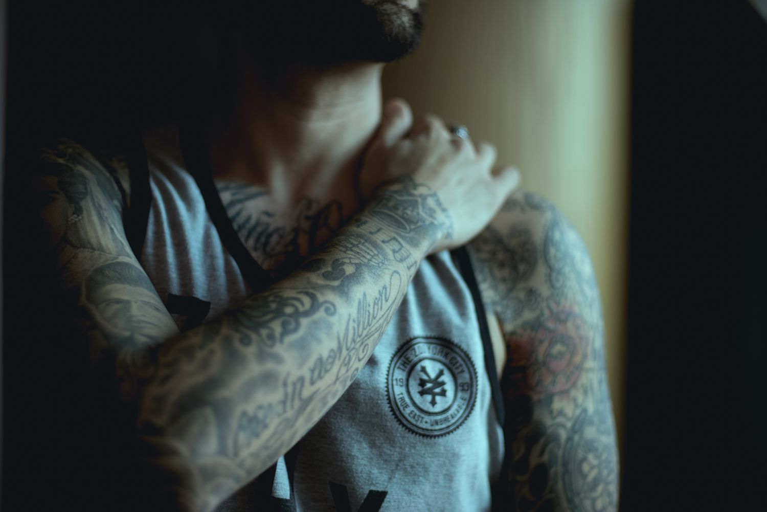 Artistic shot of detailed arm tattoos and grey athletic wear in natural window lighting.