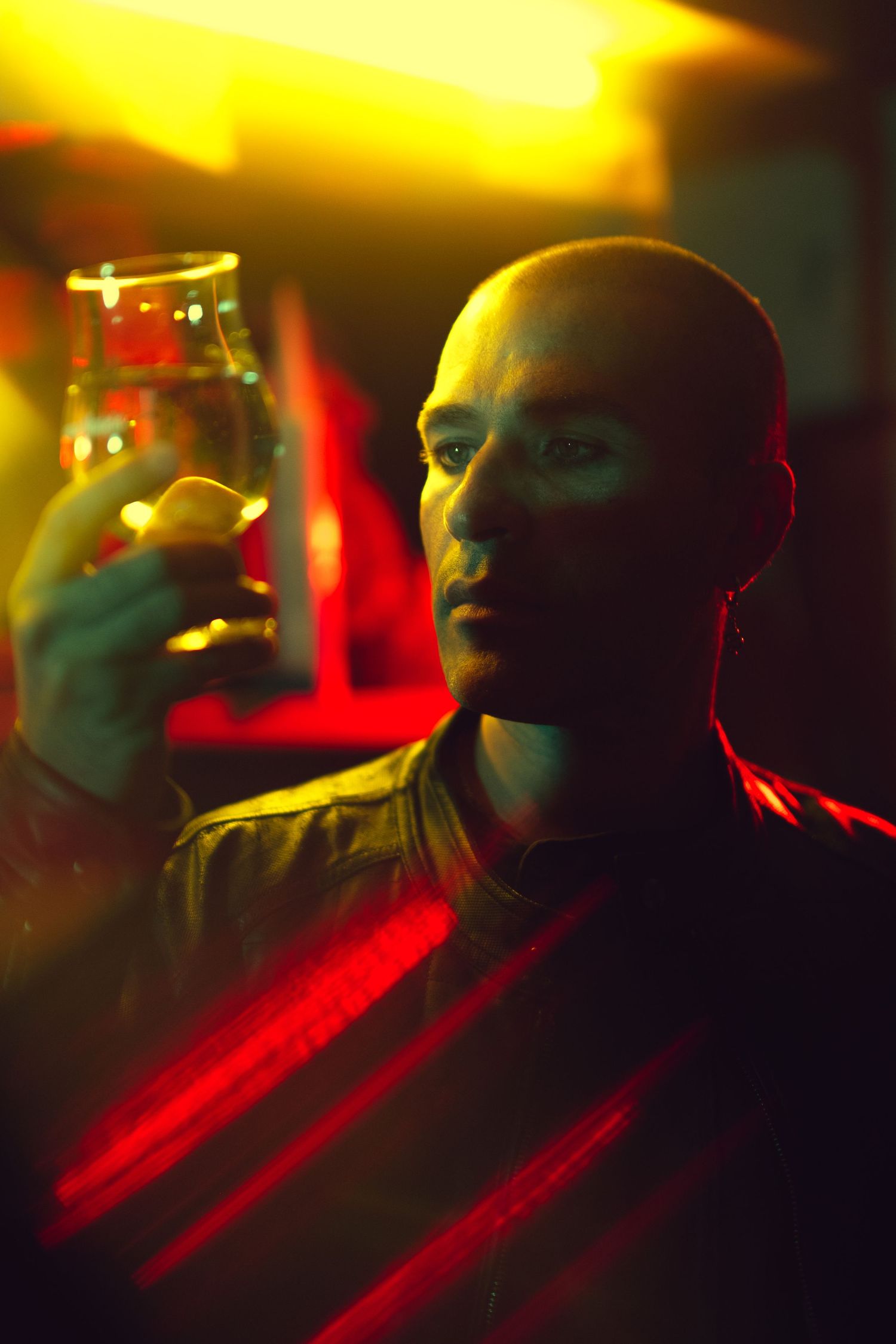 A person holds up a glass in moody lighting with red and yellow neon colors creating a dramatic atmosphere.