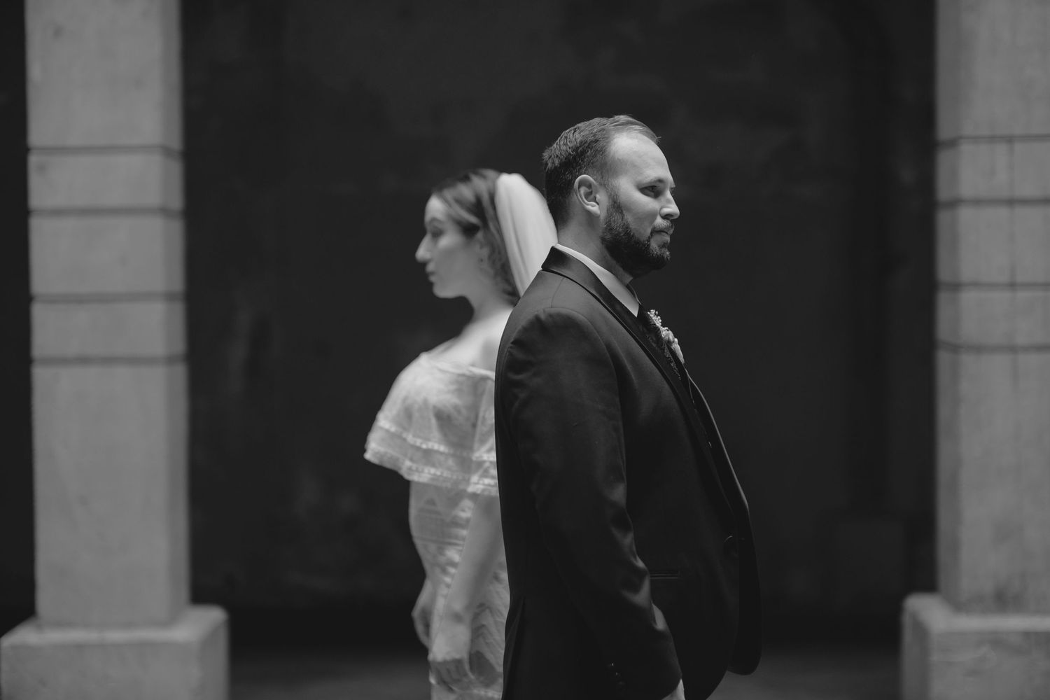 Artistic black and white portrait of couple standing back-to-back in formal attire.