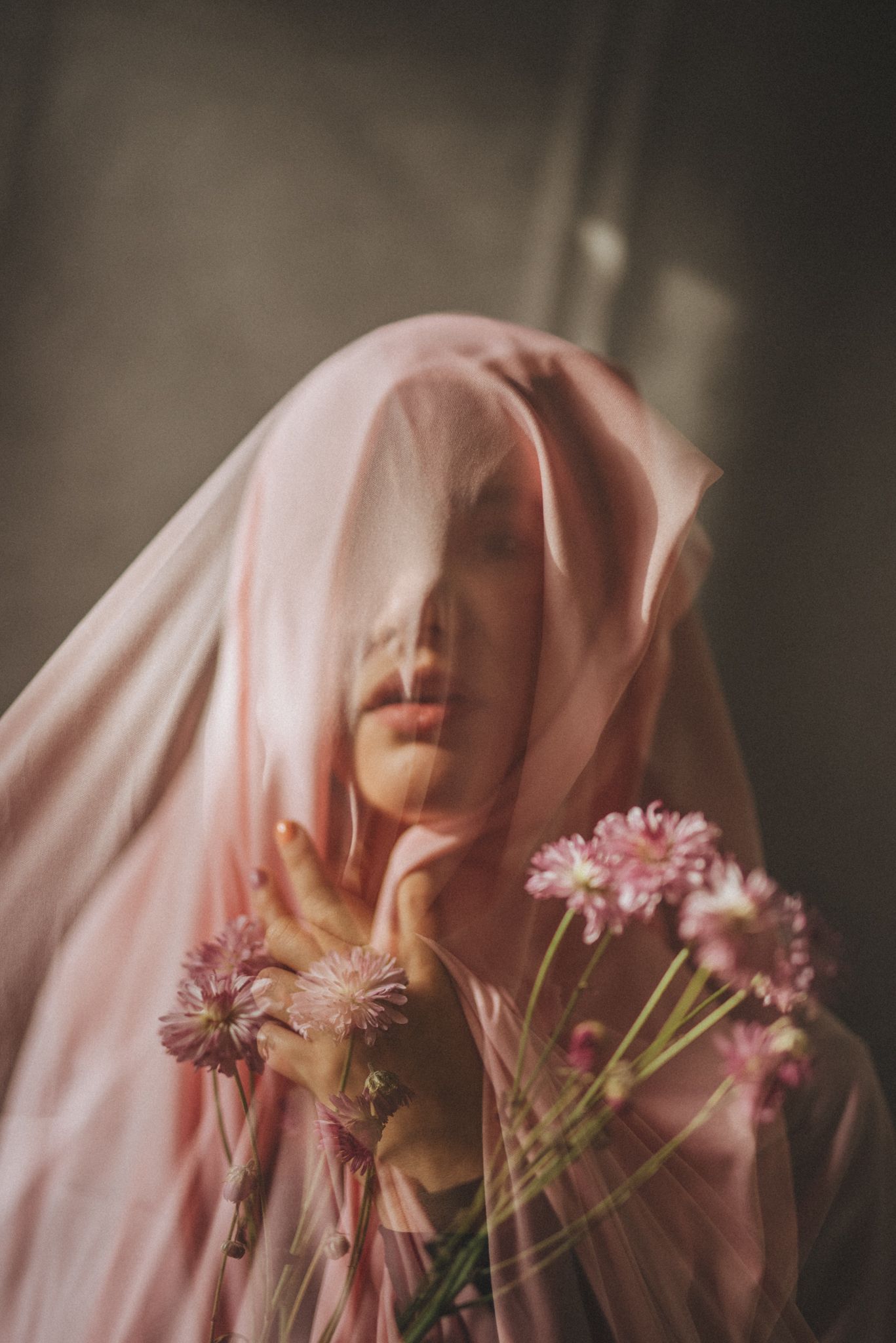 Dreamy portrait of figure in pink veil holding pink flowers.