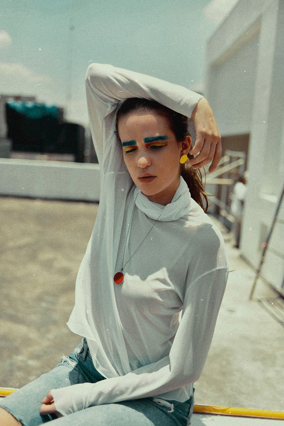 Modern portrait of person in white turtleneck with blue eye makeup against urban backdrop.