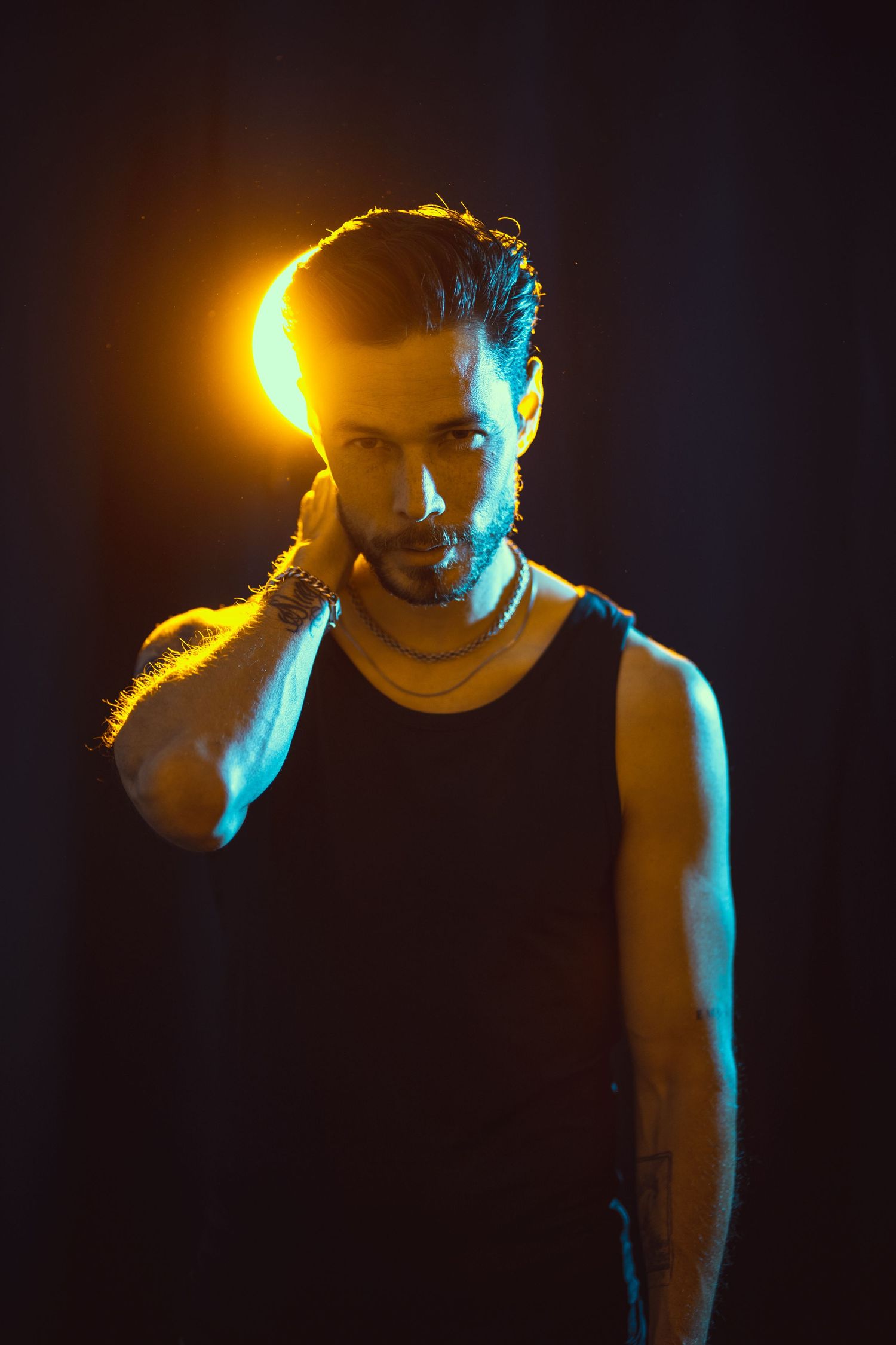 Dramatic portrait with golden rim lighting and blue highlights against dark background.