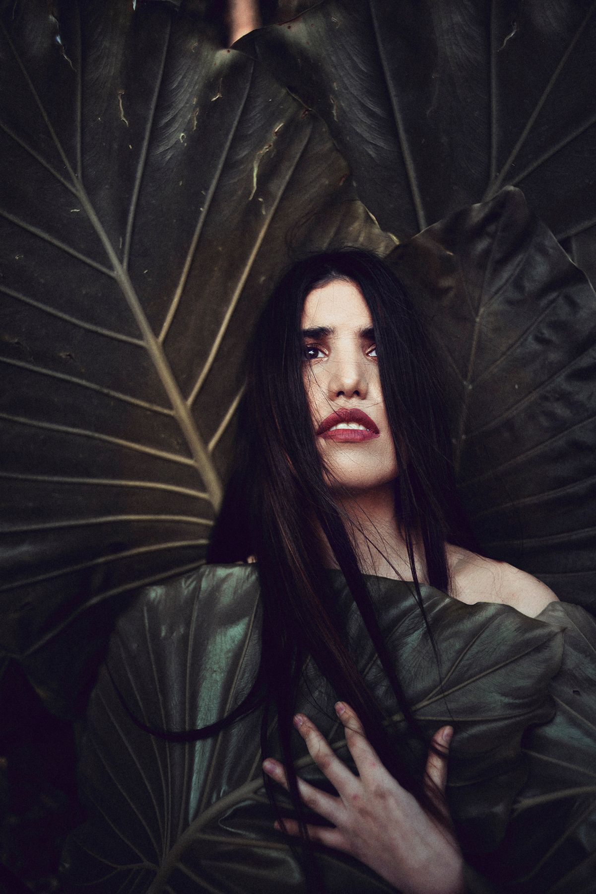 Dramatic portrait against large dark leaves in moody lighting.