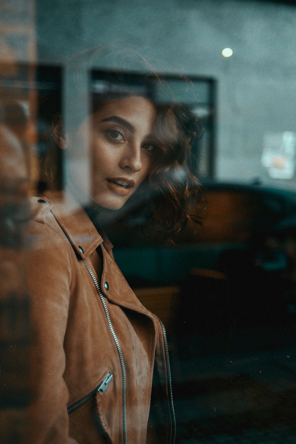 Artistic portrait through glass showing reflection in brown leather jacket.