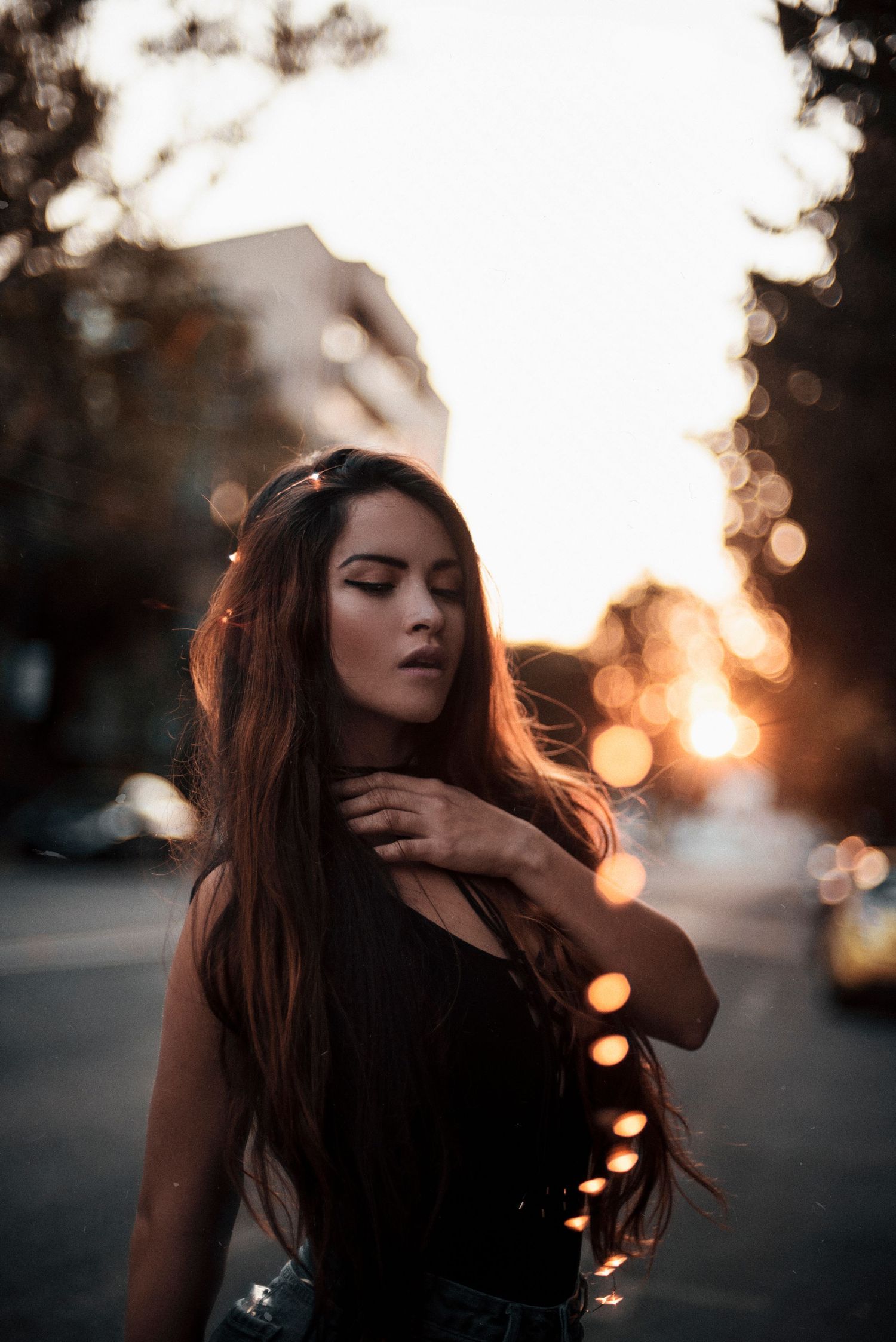 Moody sunset portrait with bokeh lights and dramatic shadows on an urban street.