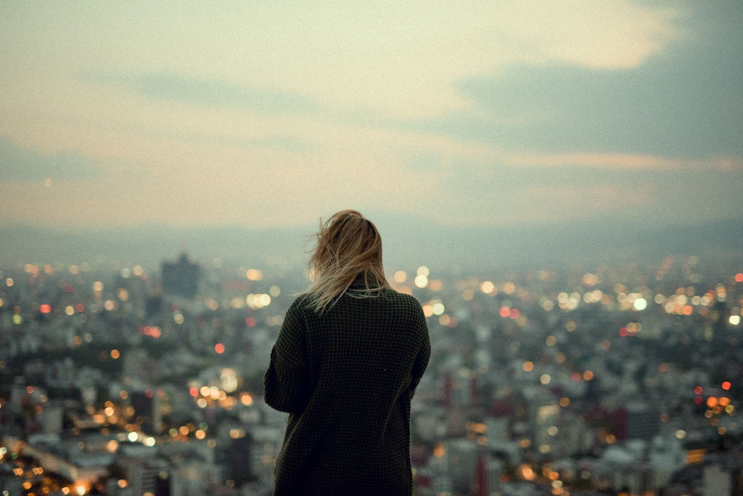 Silhouetted figure looking out over city skyline at dusk.