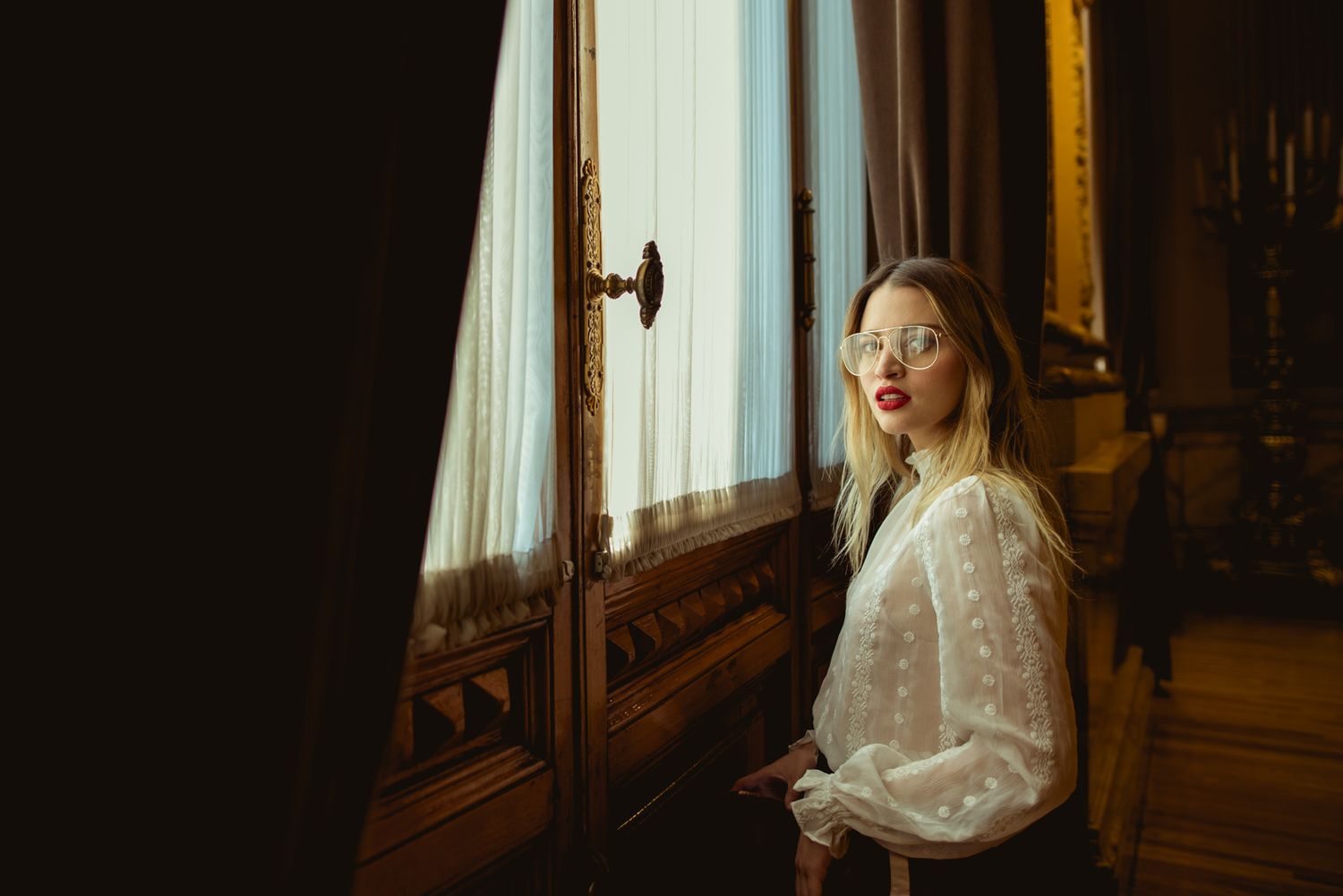 Dreamy portrait of woman in white blouse by vintage window with natural light.