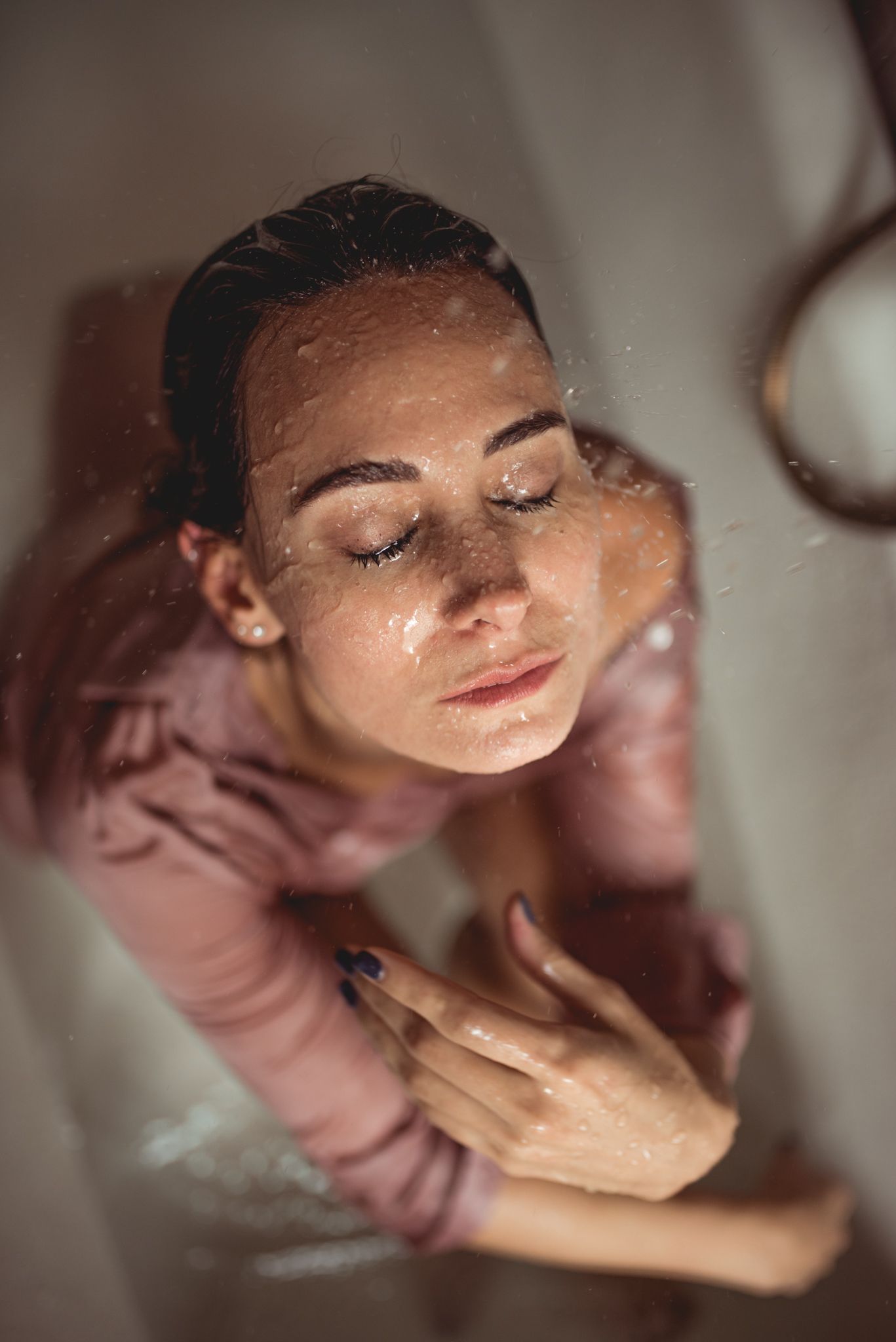Artistic portrait of person in pink shirt with closed eyes and serene expression in soft lighting.