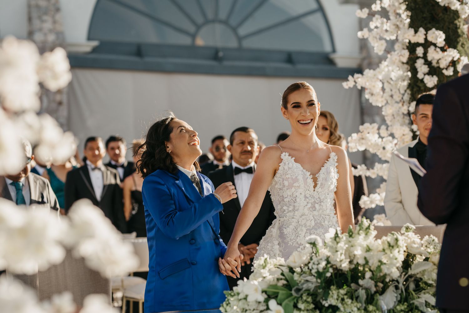 An outdoor wedding ceremony with elegant white floral decorations and guests in formal attire.