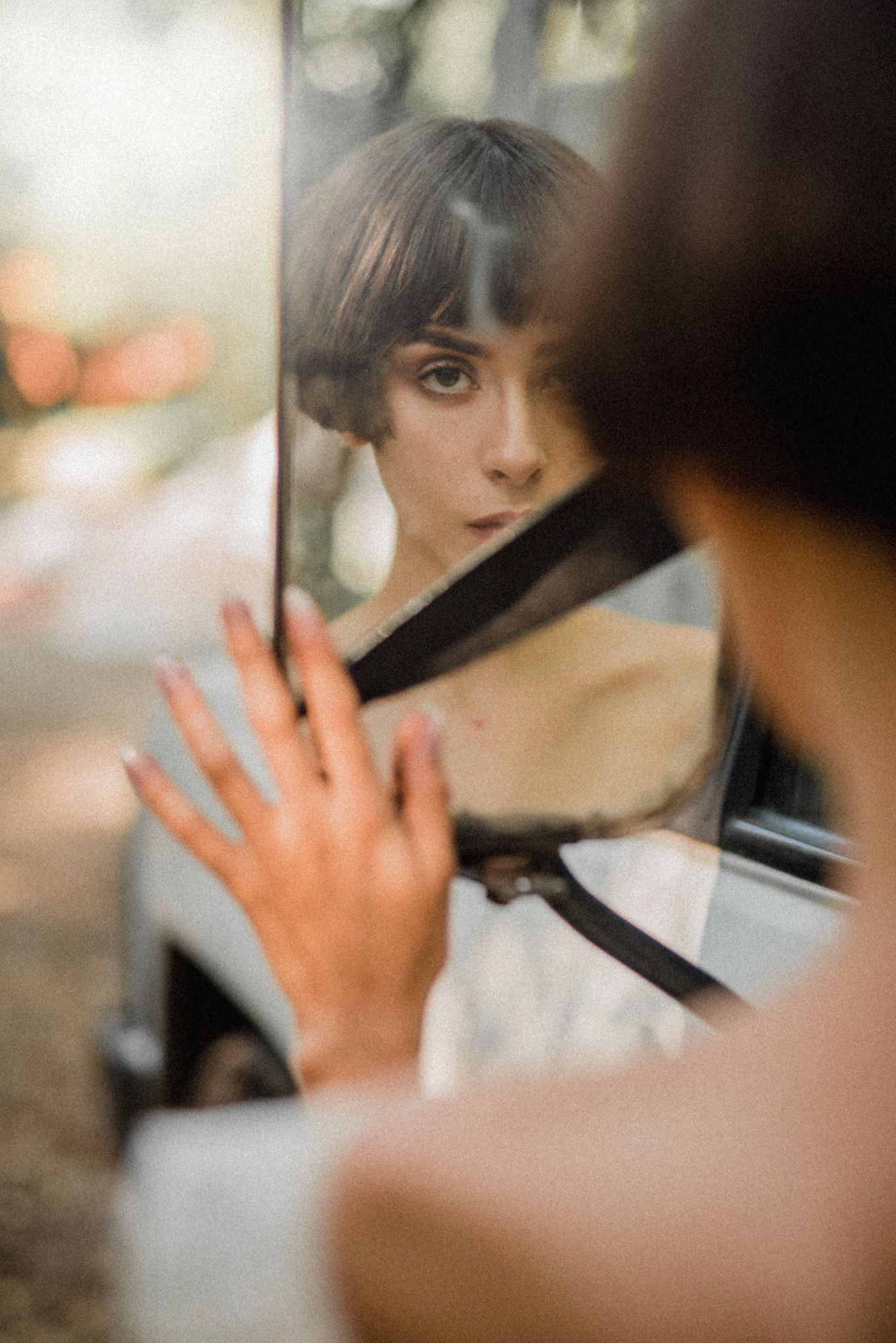 Reflection in car mirror showing vintage-inspired portrait and reaching hand.
