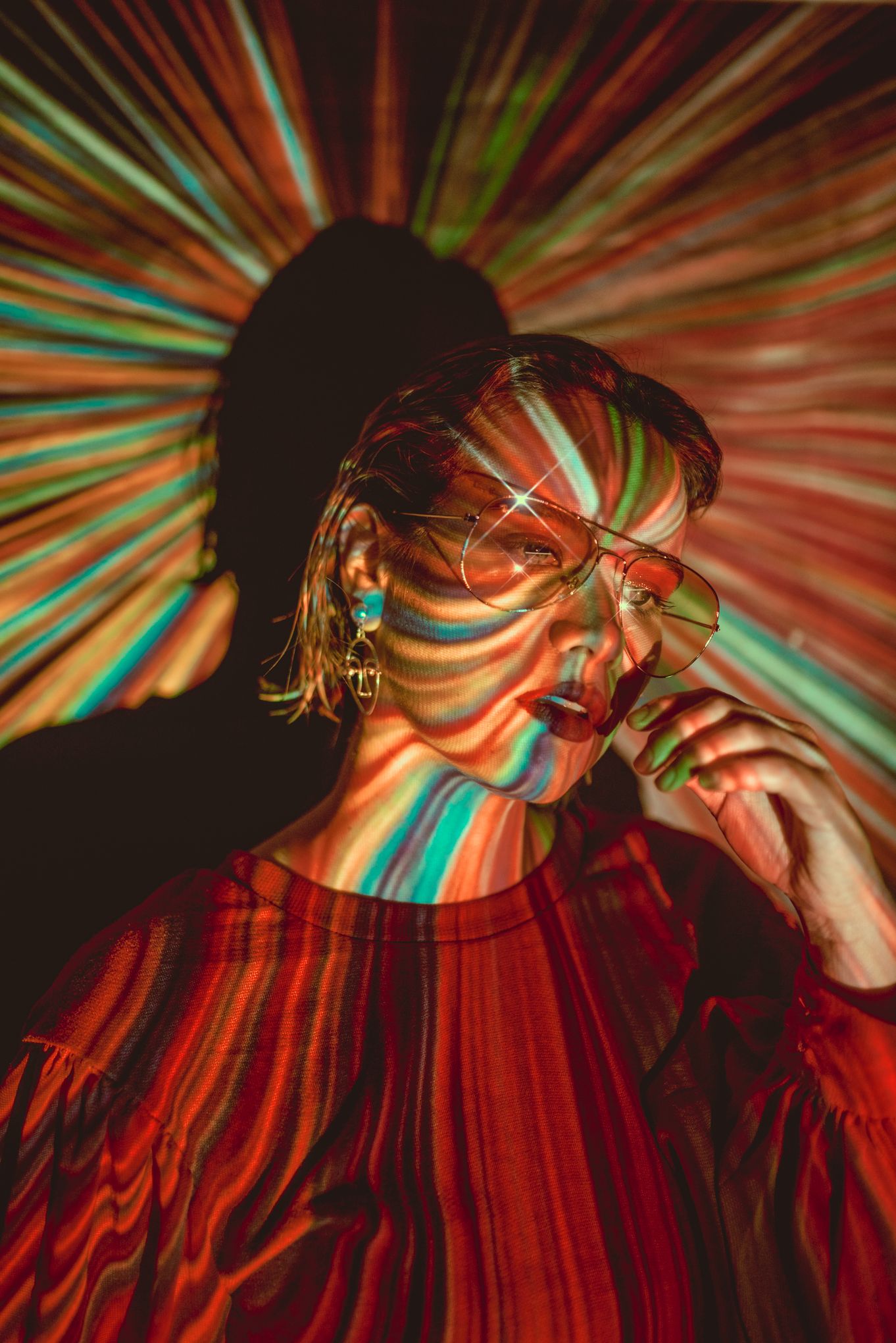 Creative portrait with colorful light projections creating striped patterns across the subject's face in red and turquoise tones.