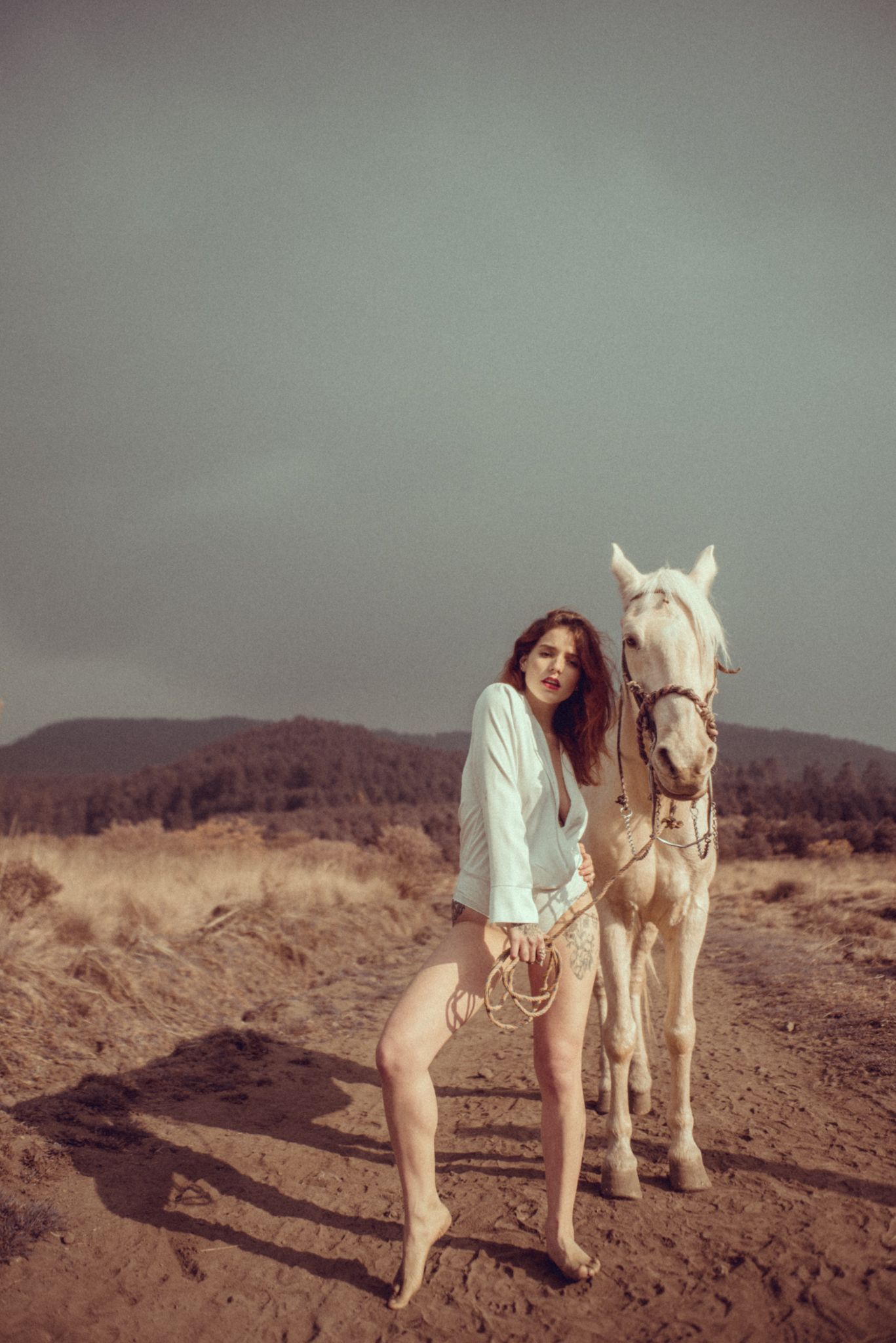 A person poses playfully with a white horse in an outdoor desert setting.