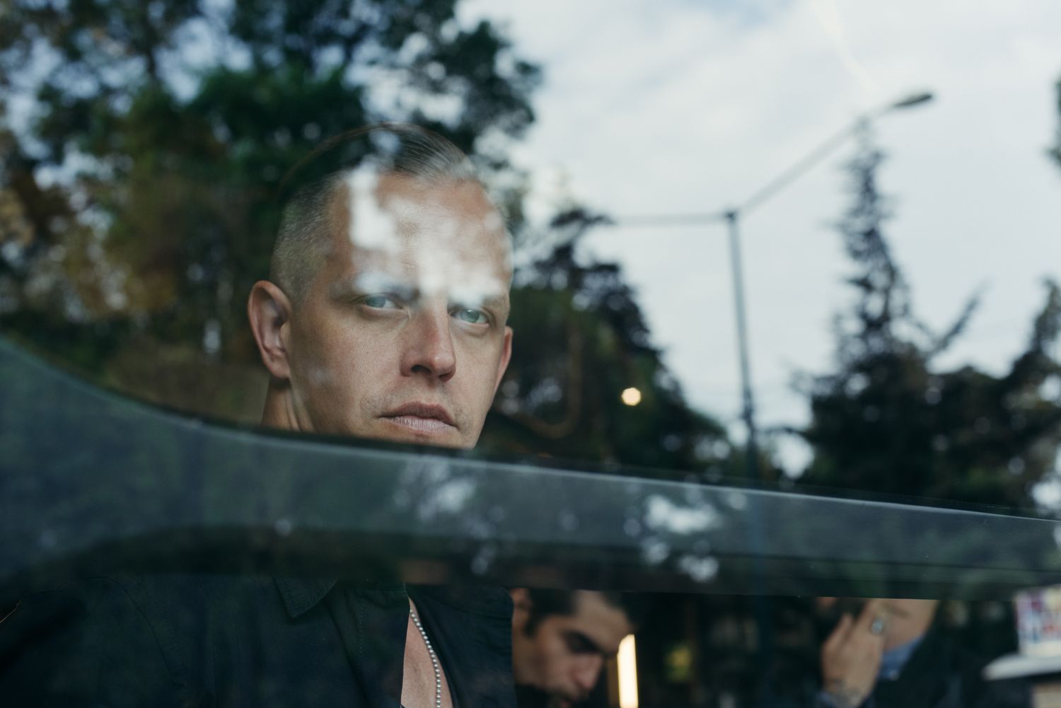 Profile view through car window with reflective glass creating atmospheric urban scene.