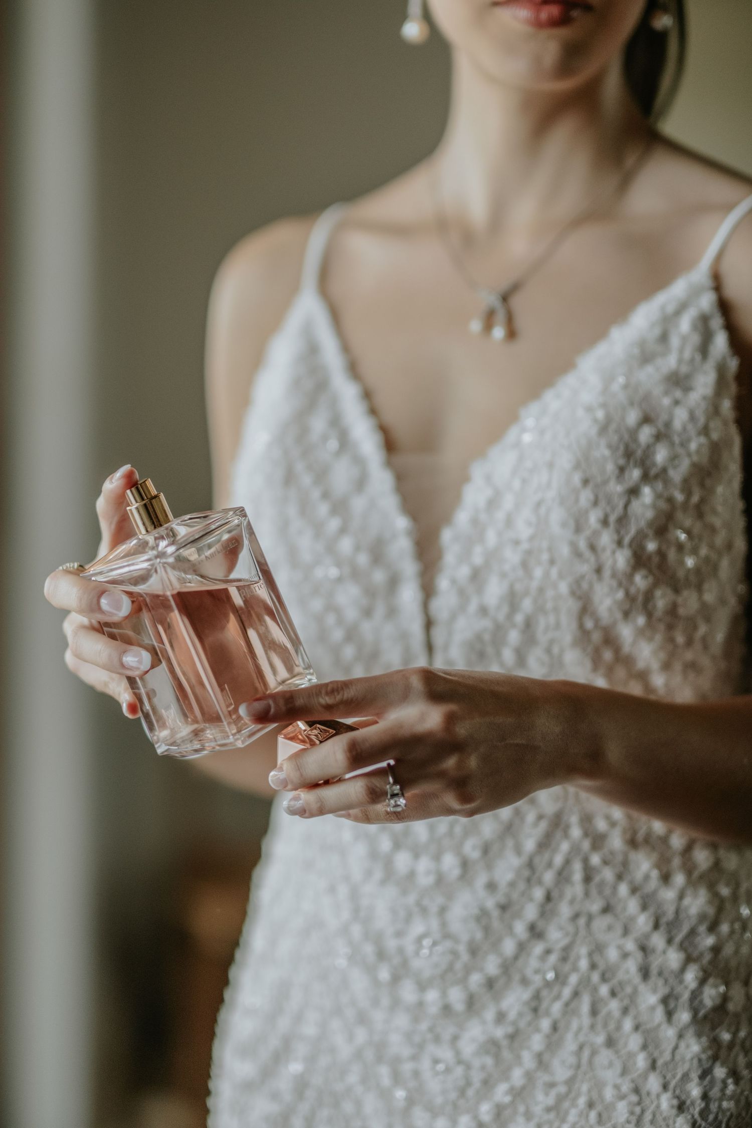 Elegant hands holding a crystal perfume bottle while wearing a detailed white wedding gown.