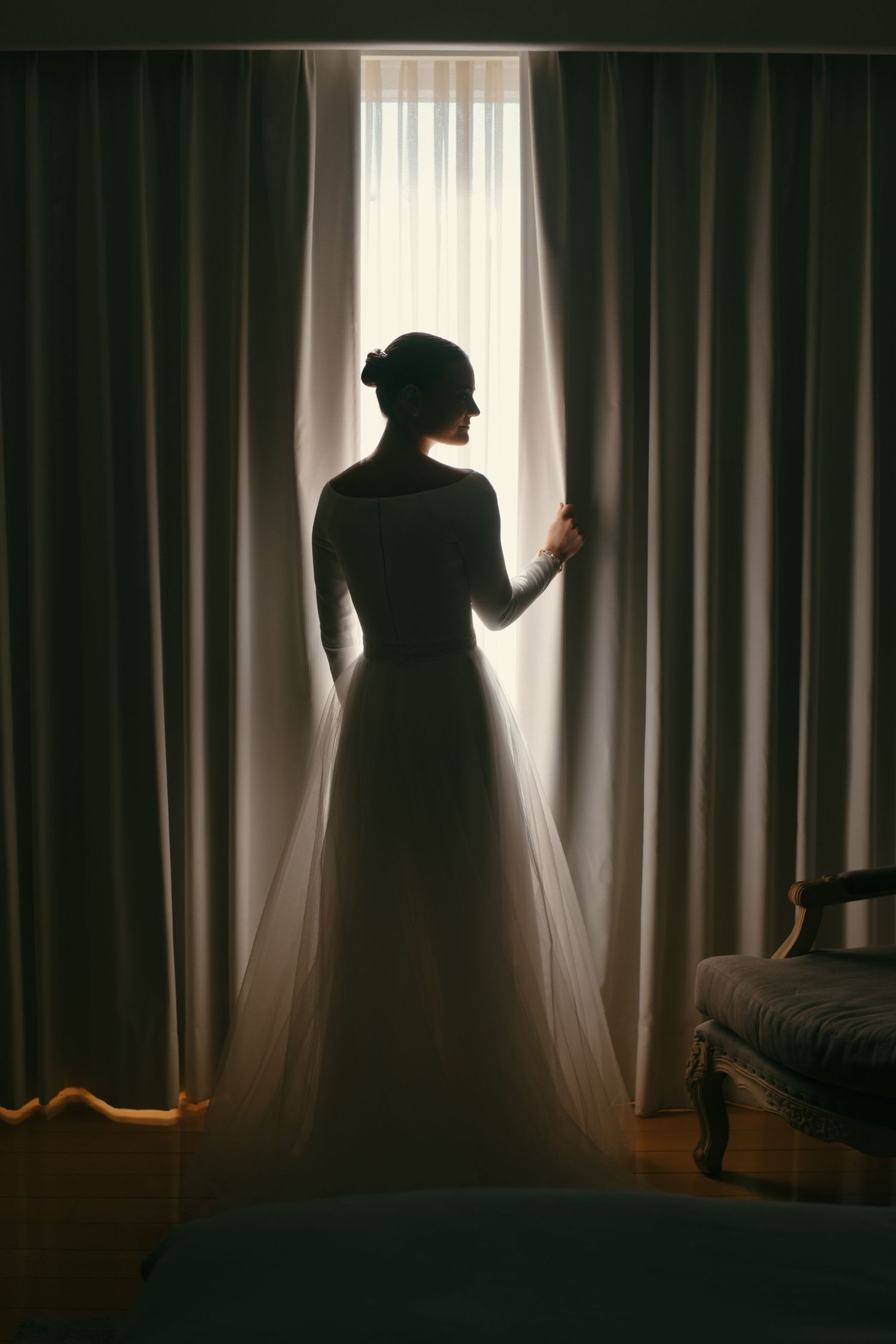 A silhouetted figure in an elegant dress stands at a window, backlit by soft light filtering through curtains.