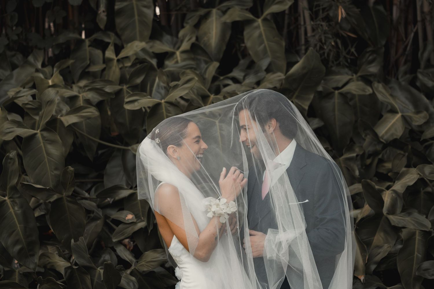 Two wedding figures create an intimate moment together while enveloped under a romantic white veil.