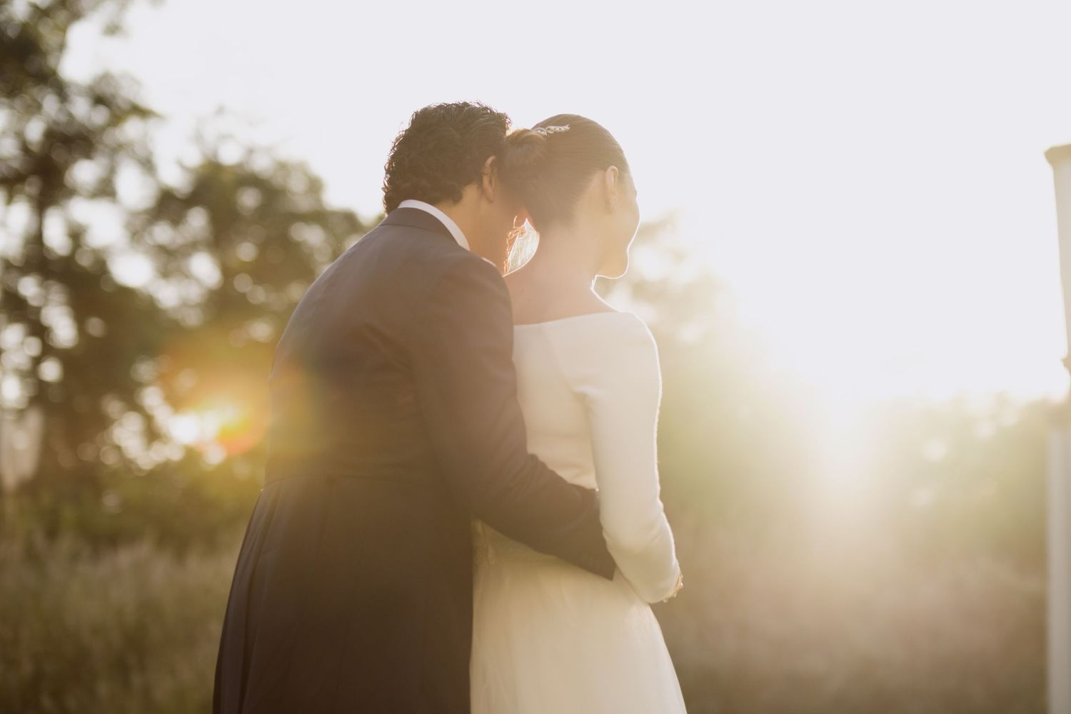 Intimate wedding moment captured in warm sunlight with lens flare.