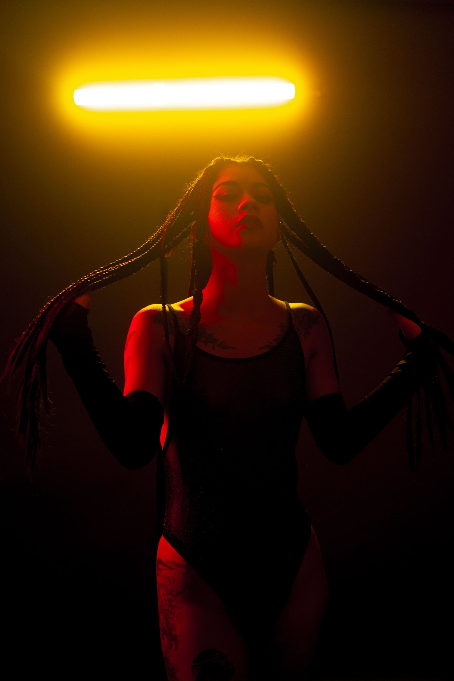 Dramatic silhouette of a figure in black dance attire illuminated by warm yellow lighting from above and red accent lights.