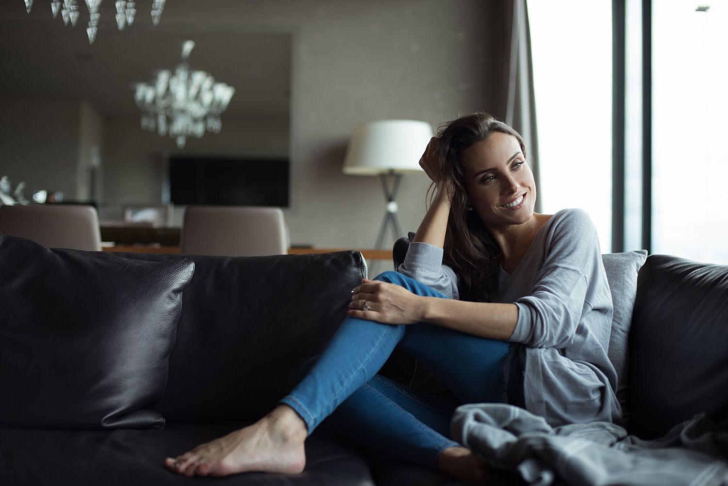 Relaxed person lounging on dark couch near window with natural lighting.