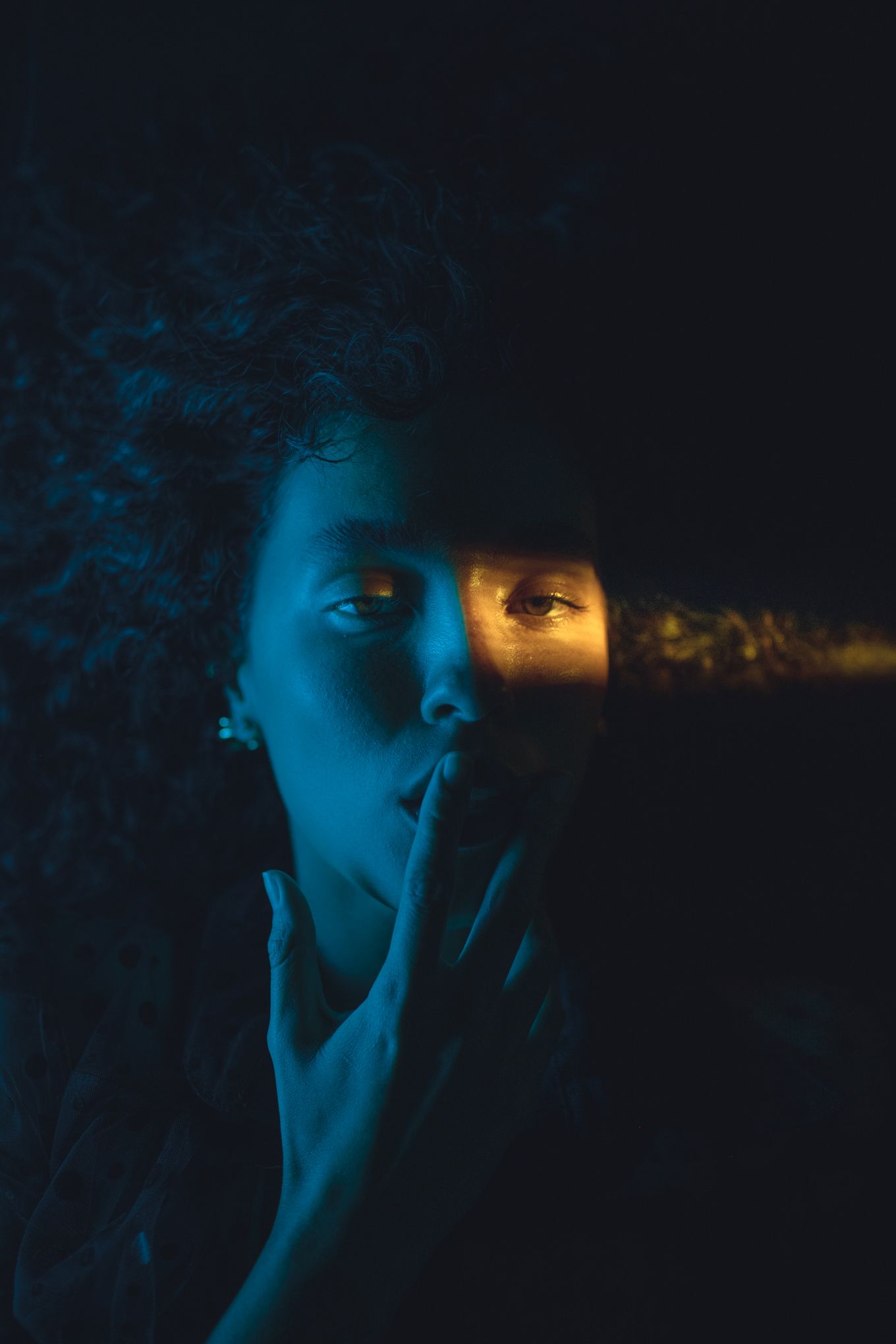 Atmospheric portrait with finger on lips illuminated by blue and orange lighting.