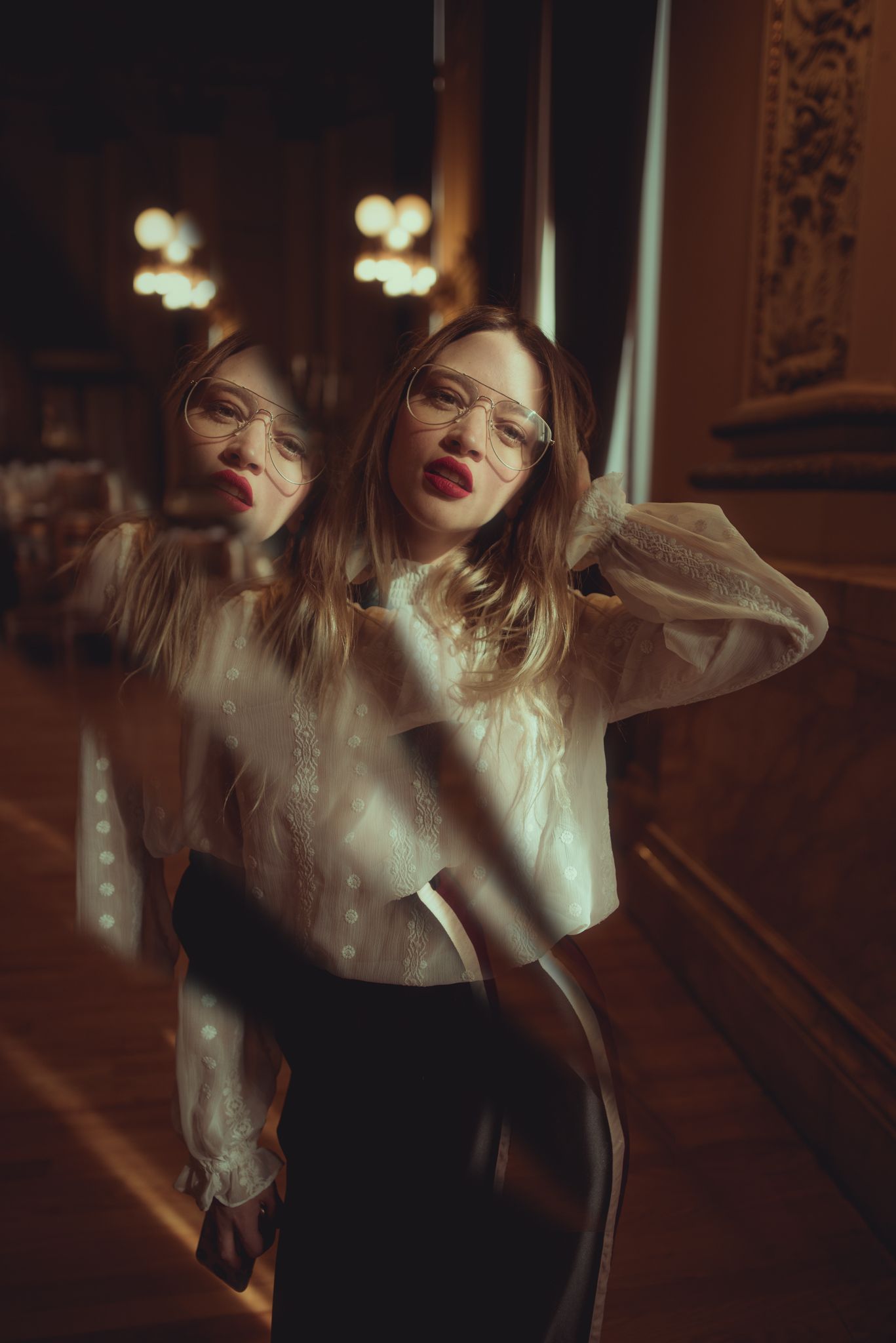 Artistic portrait in vintage setting with soft lighting and reflective surface showing dramatic pose in Victorian style blouse.