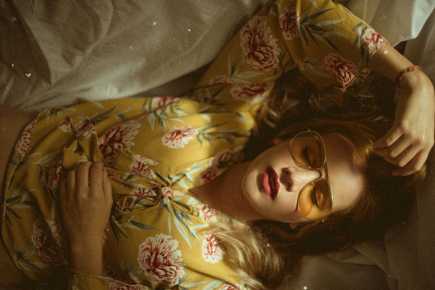 Artistic portrait of person lying down wearing floral silk dress in warm golden tones.