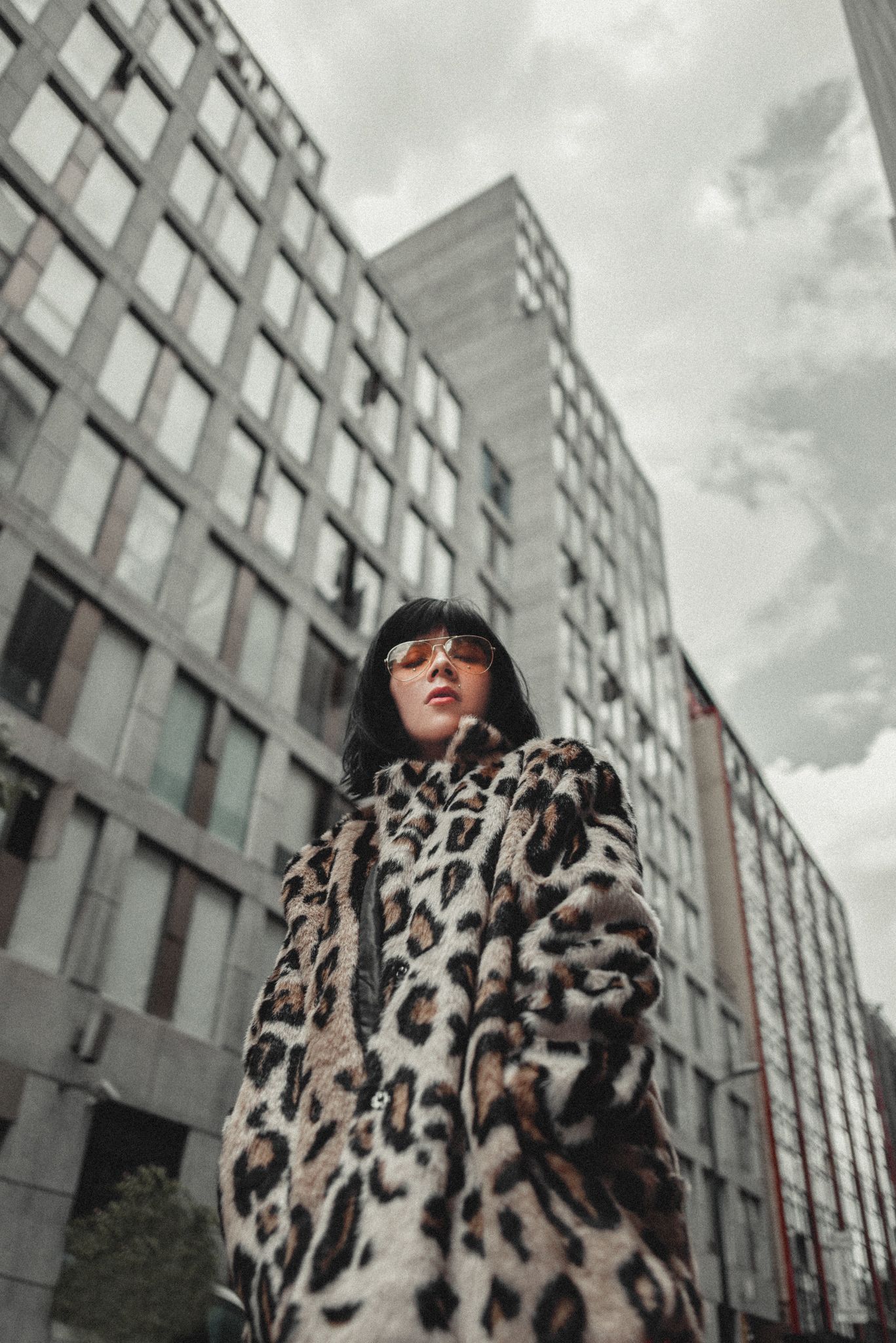 Low angle portrait of woman in leopard print coat against modern architecture.