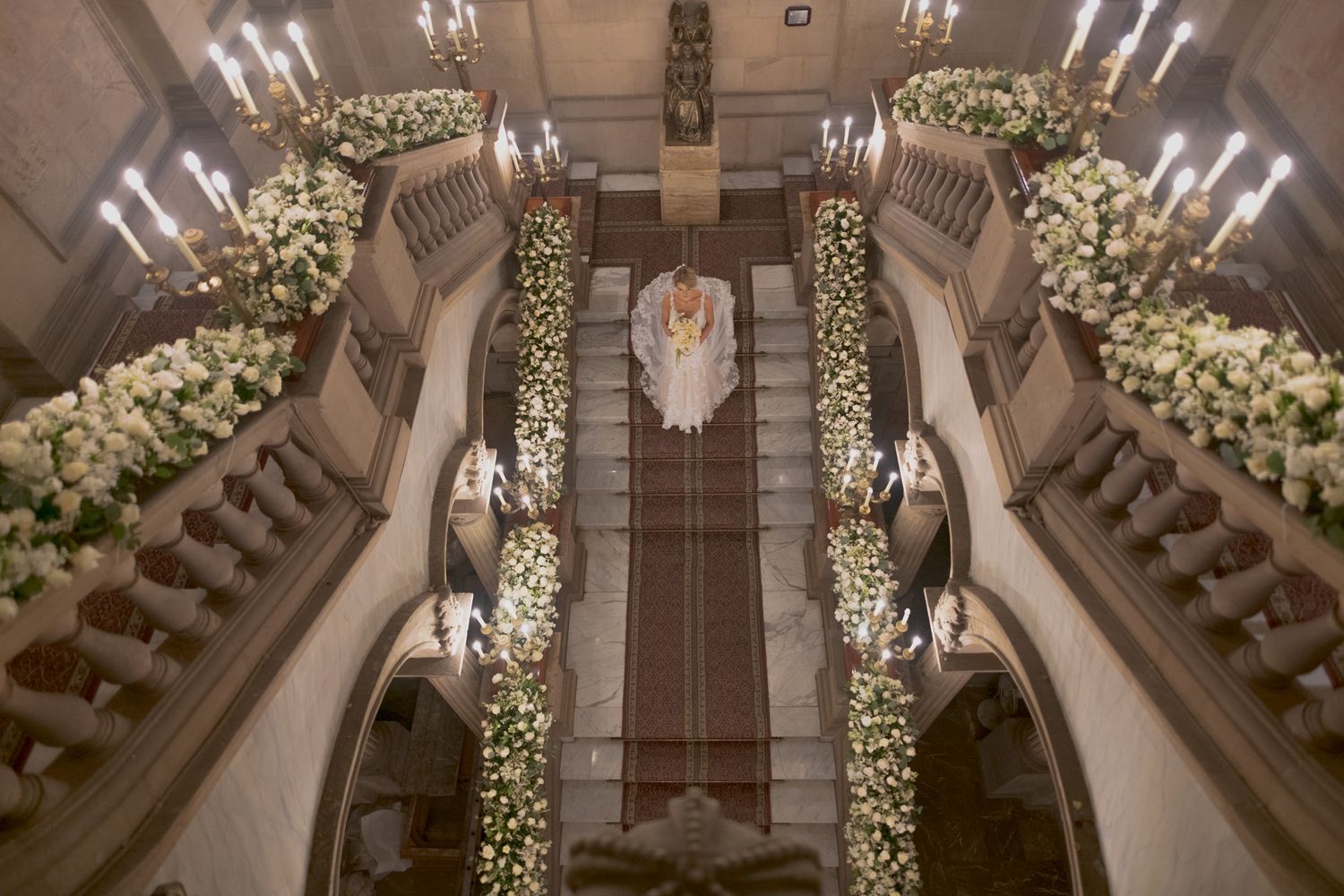 Aerial view of grand staircase decorated with white floral arrangements and candles for wedding ceremony.
