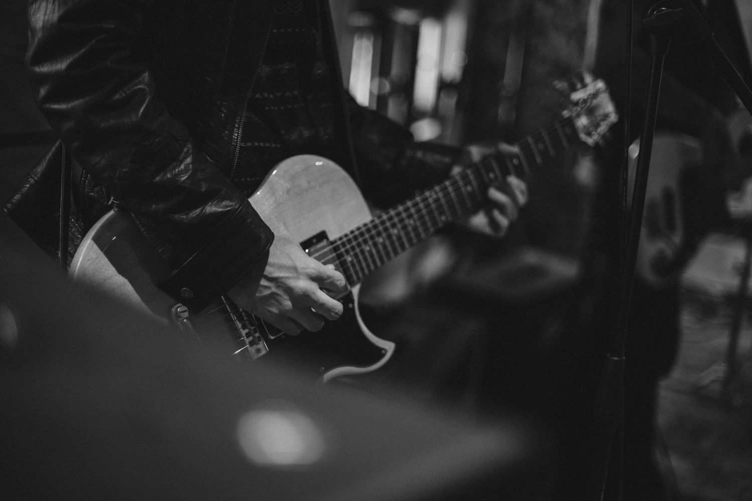 Black and white image showing hands playing acoustic guitar with shallow depth of field.