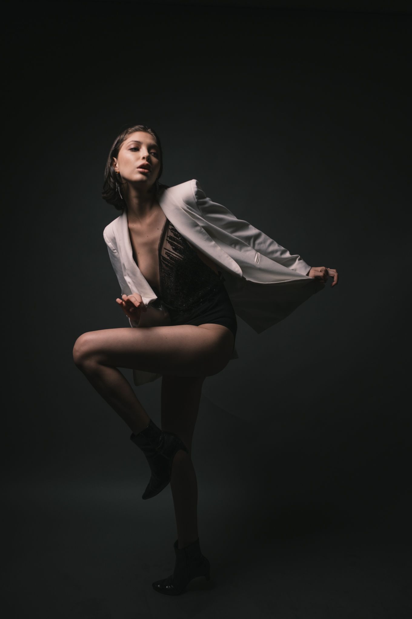 Dramatic dance pose in white flowing jacket against black background.