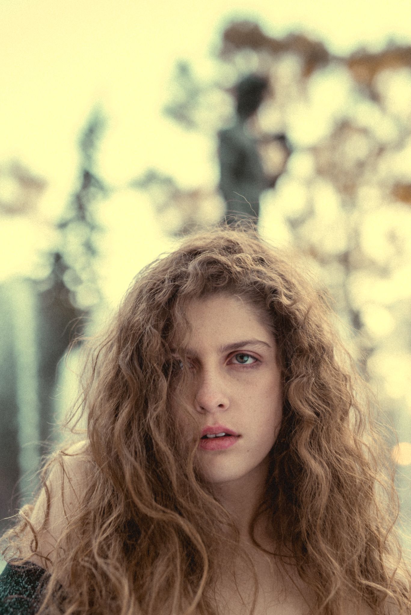 Dramatic portrait with voluminous curly hair against yellow-tinted background.