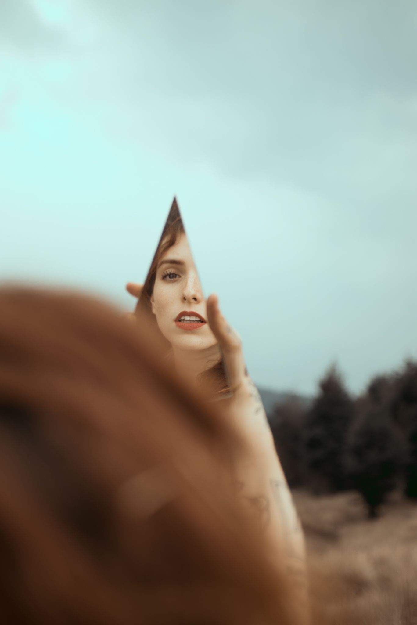 Ethereal portrait through broken mirror fragments in nature with soft focus.
