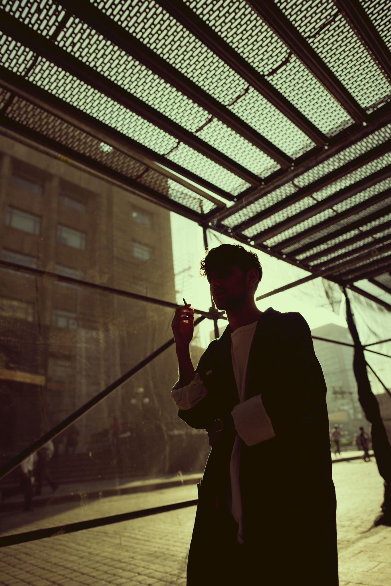Silhouette of person smoking under geometric ceiling with backlit green lighting.