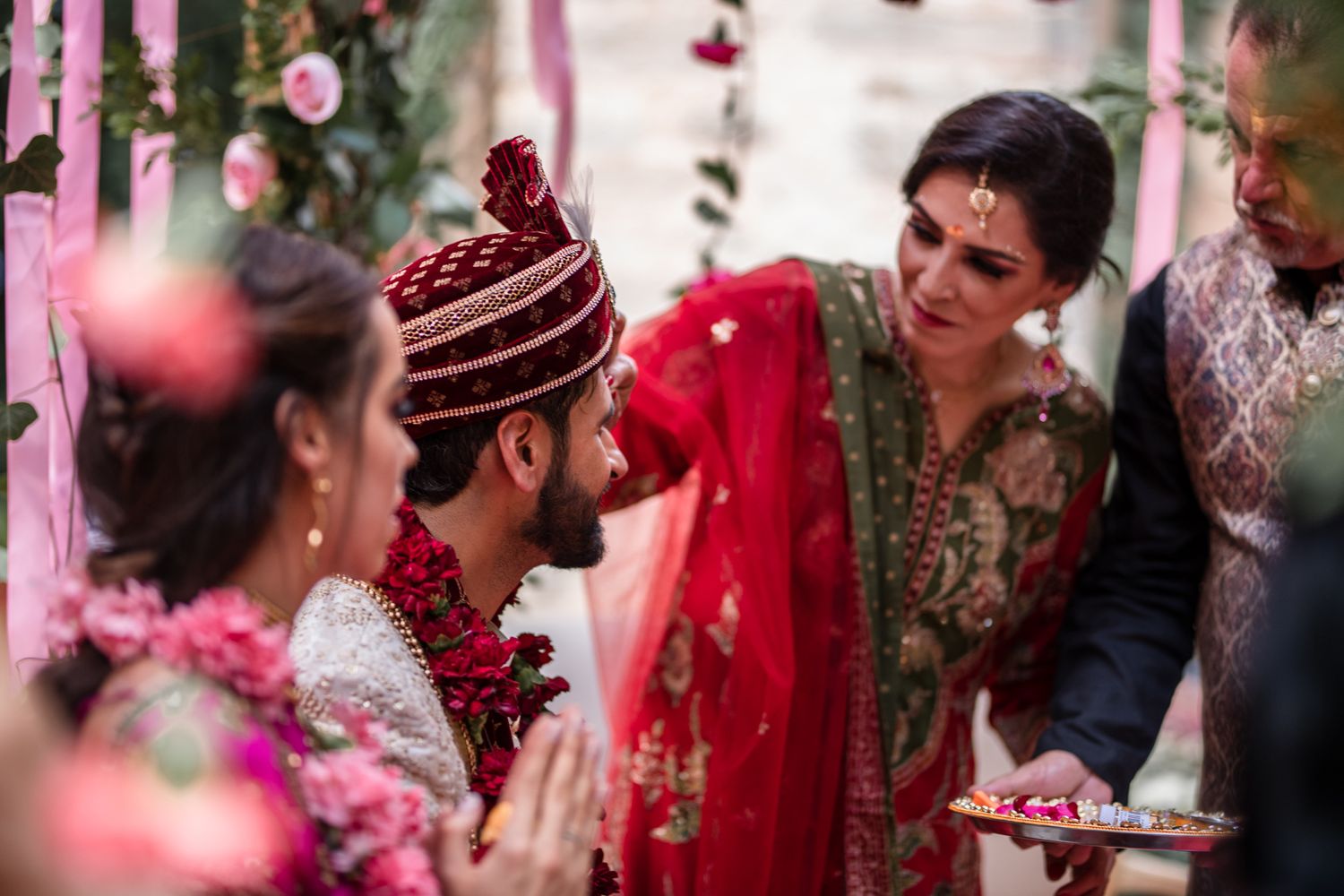 Guests at a traditional Indian wedding ceremony share joyful moments amid pink decorations and festive attire.