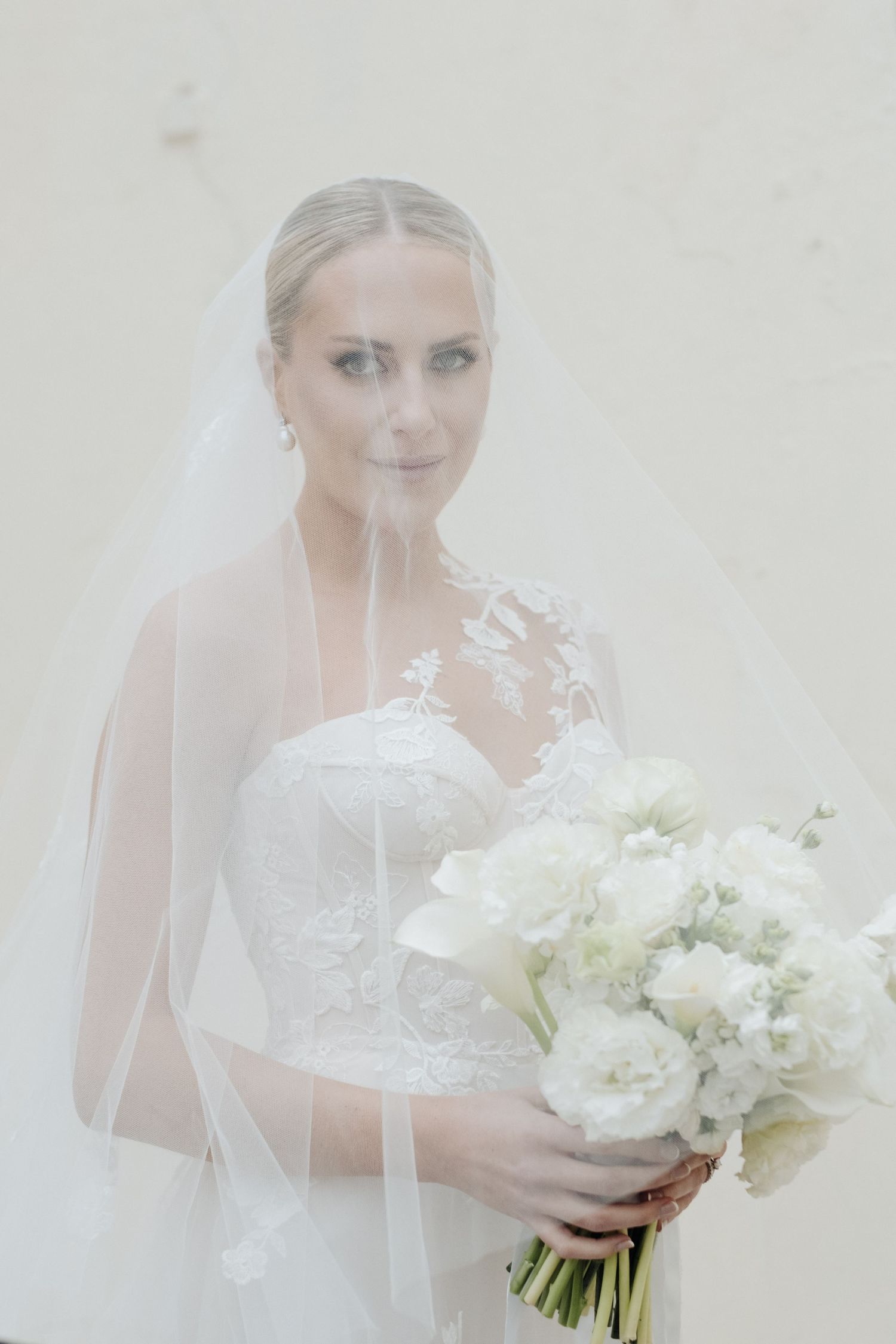 Ethereal bridal portrait with white bouquet and delicate veil in soft lighting.