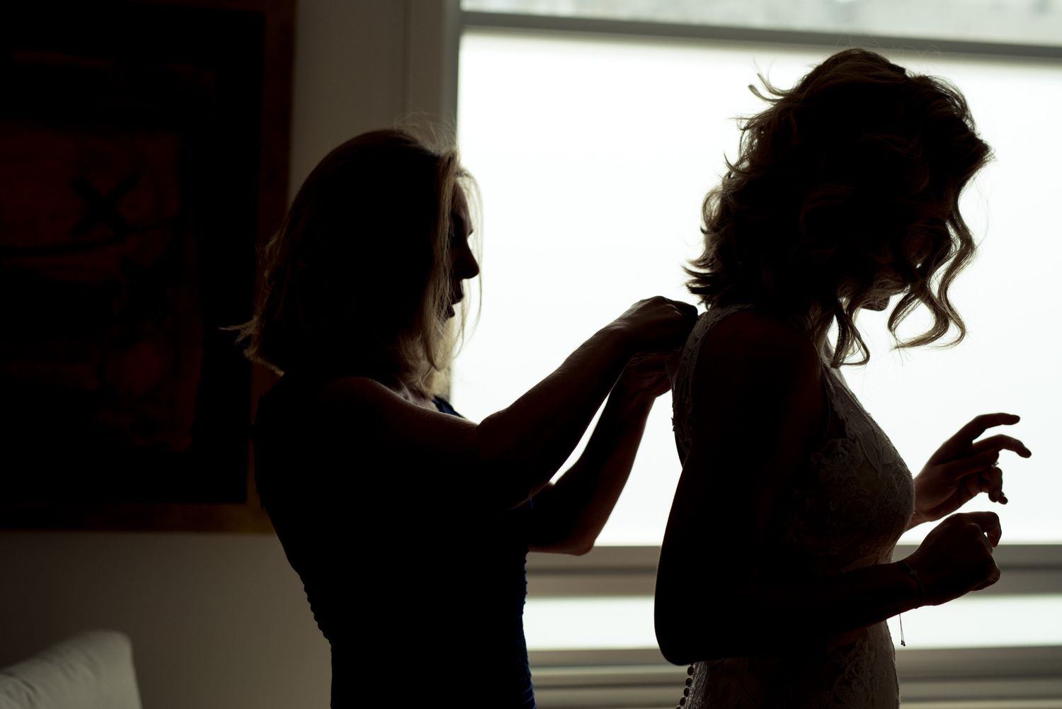 Silhouetted figures preparing for wedding ceremony against bright window.